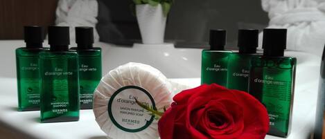 A bathroom vanity with green bottles of shampoo and soap, a white soap dish, and a red rose.