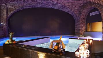 A spa area with a pool, a bar with fruit and a bottle of champagne, and candles.