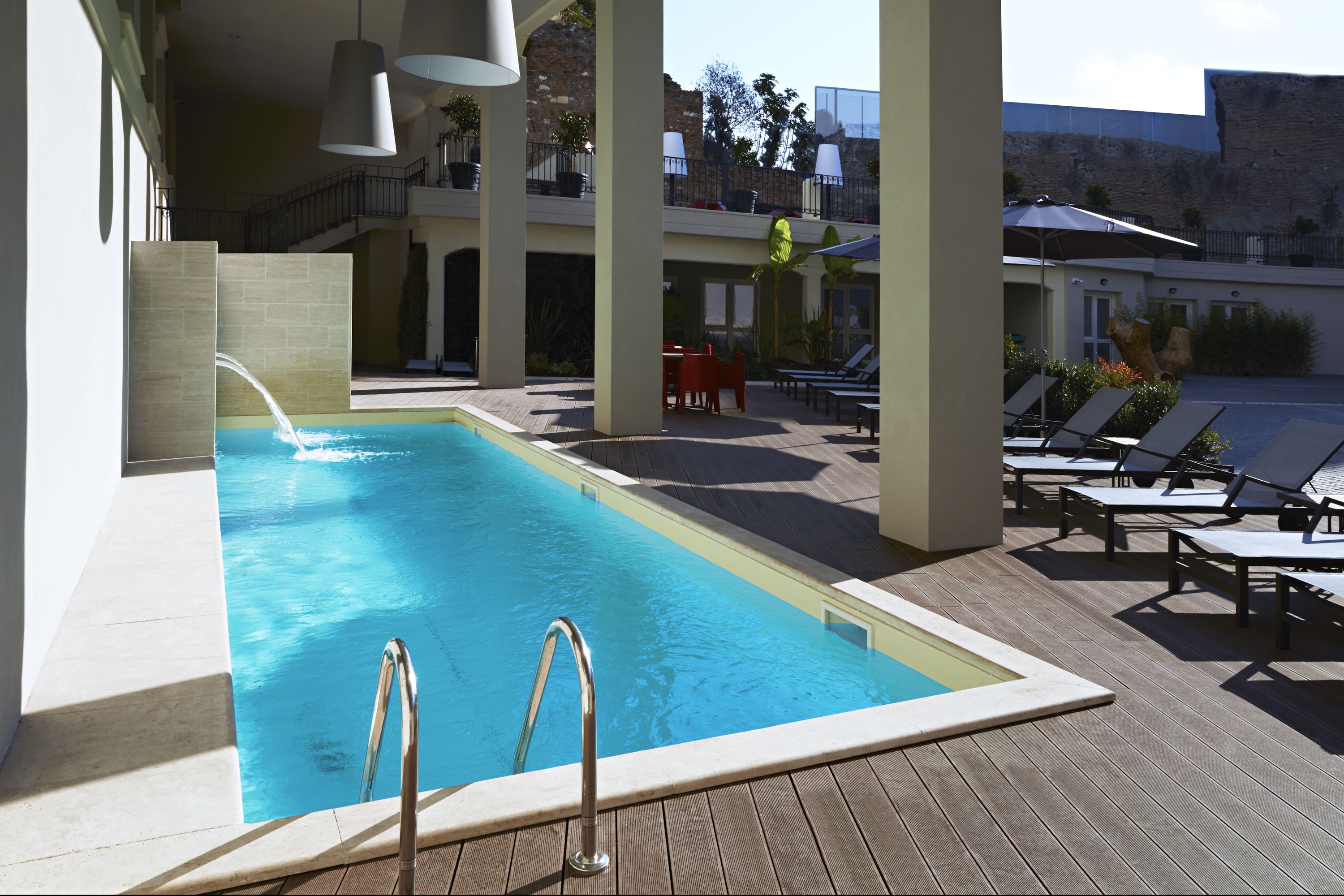 A swimming pool with a wooden deck, lounge chairs, and a view of a building with a balcony.