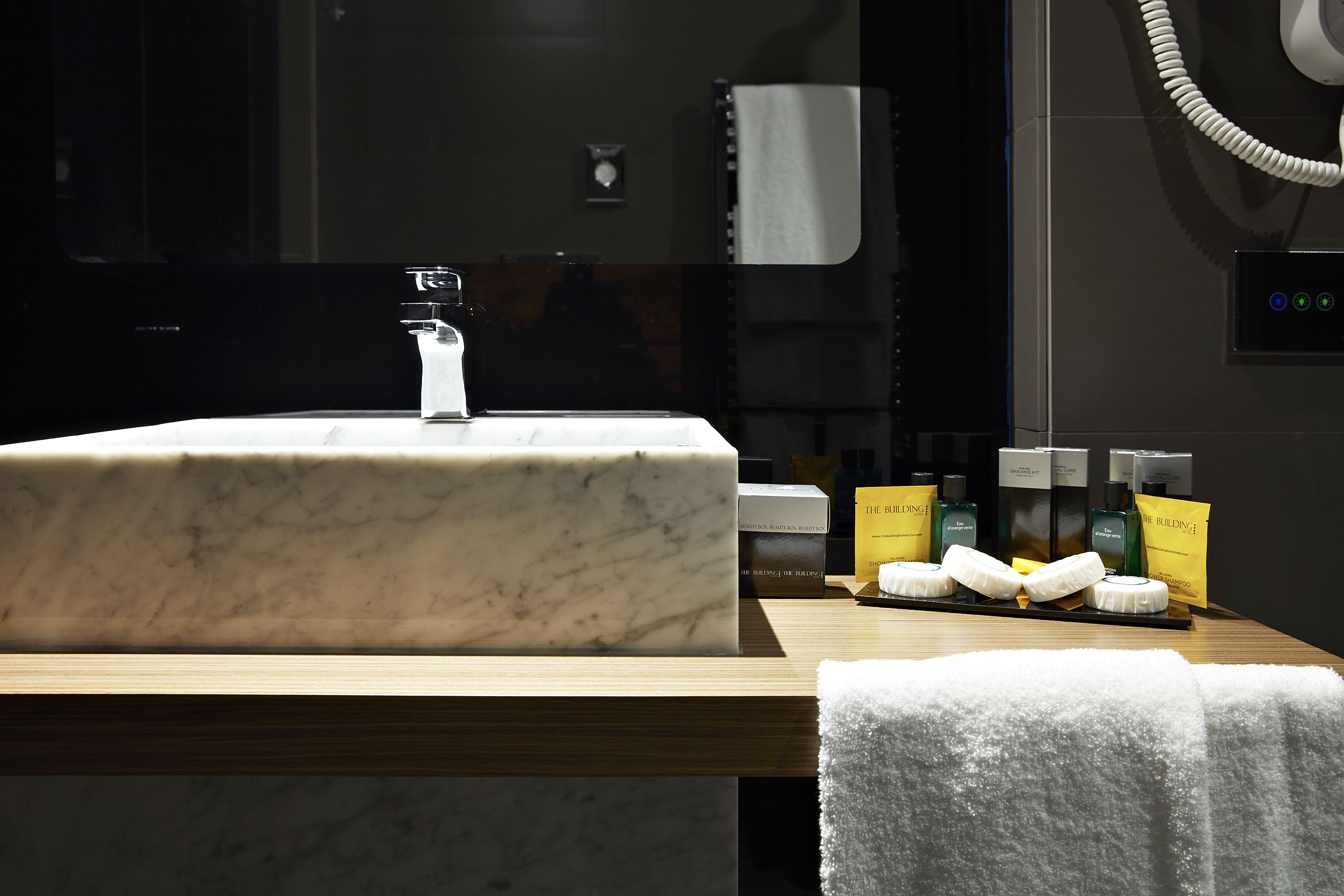 Un lavabo en marbre avec un robinet moderne, un plan de travail en bois et des articles de toilette comprenant une brosse à dents, du dentifrice et une serviette.