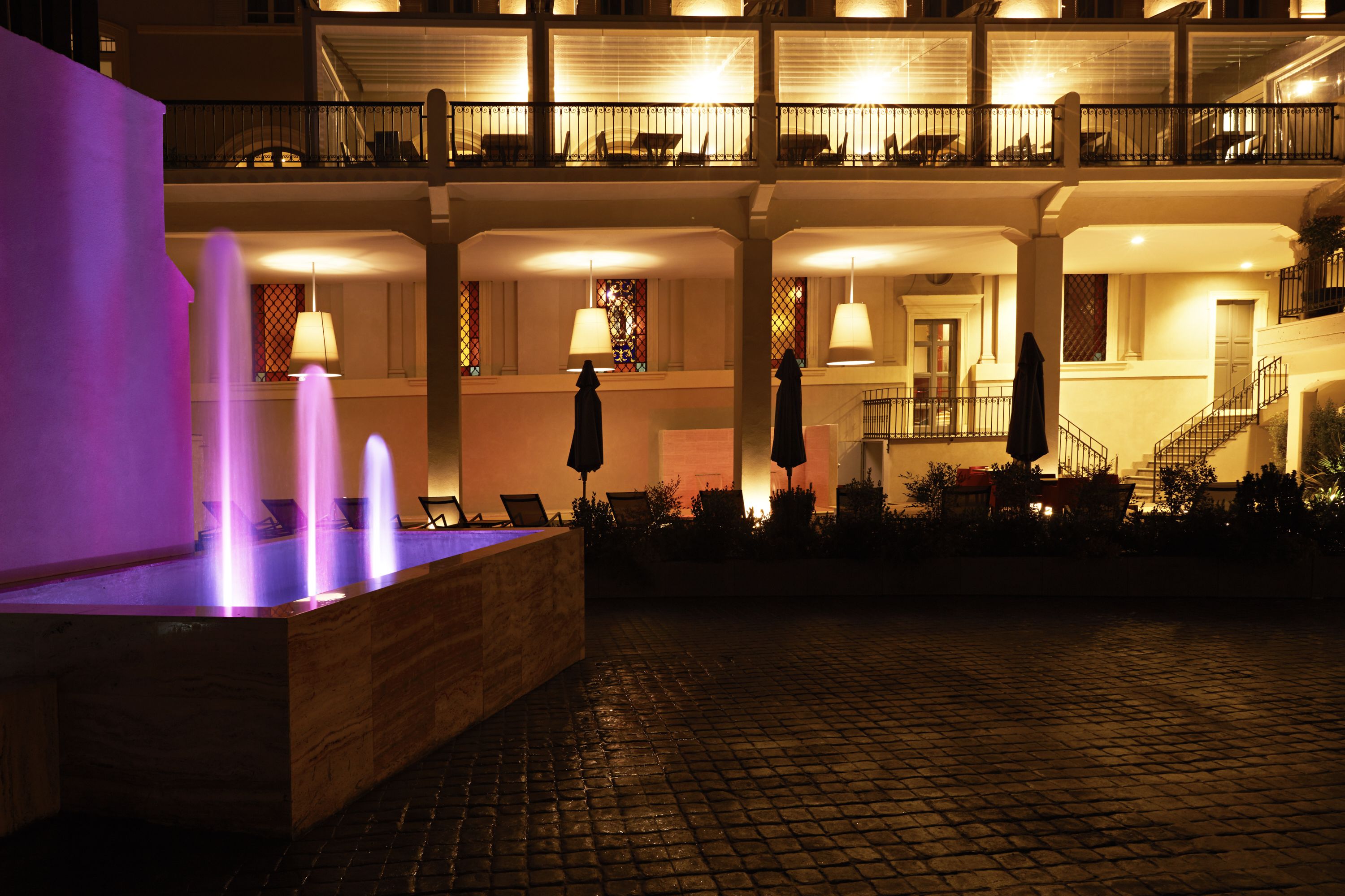 A hotel courtyard with a fountain, outdoor seating, and a staircase leading to the upper floors.