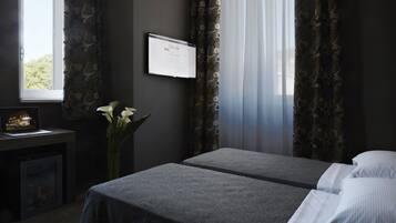 Et hotelværelse med to senge, et skrivebord med en computer, en vase med blomster og et vindue med gardiner.