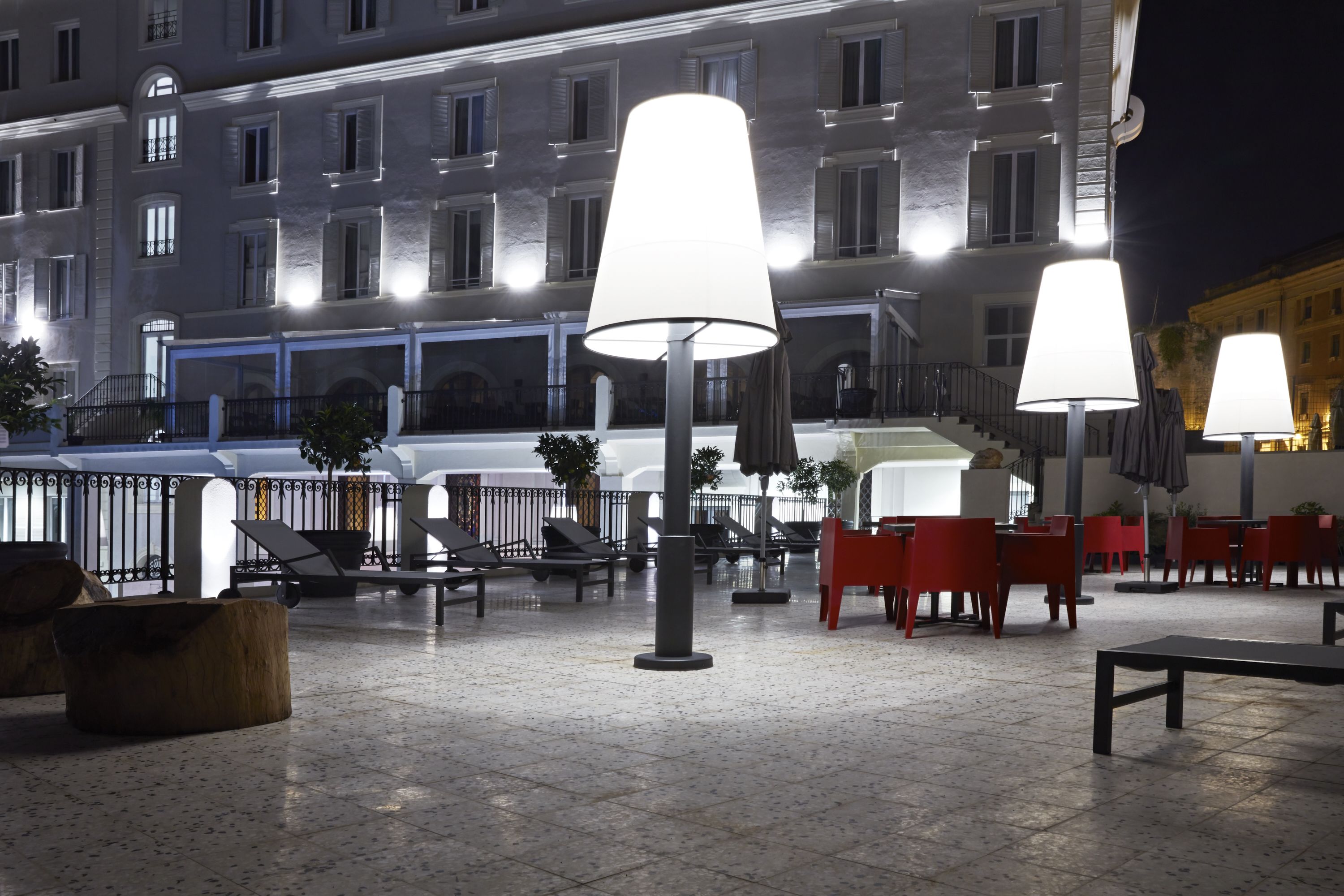 An outdoor seating area with tables and chairs, large lamps, and a building in the background.