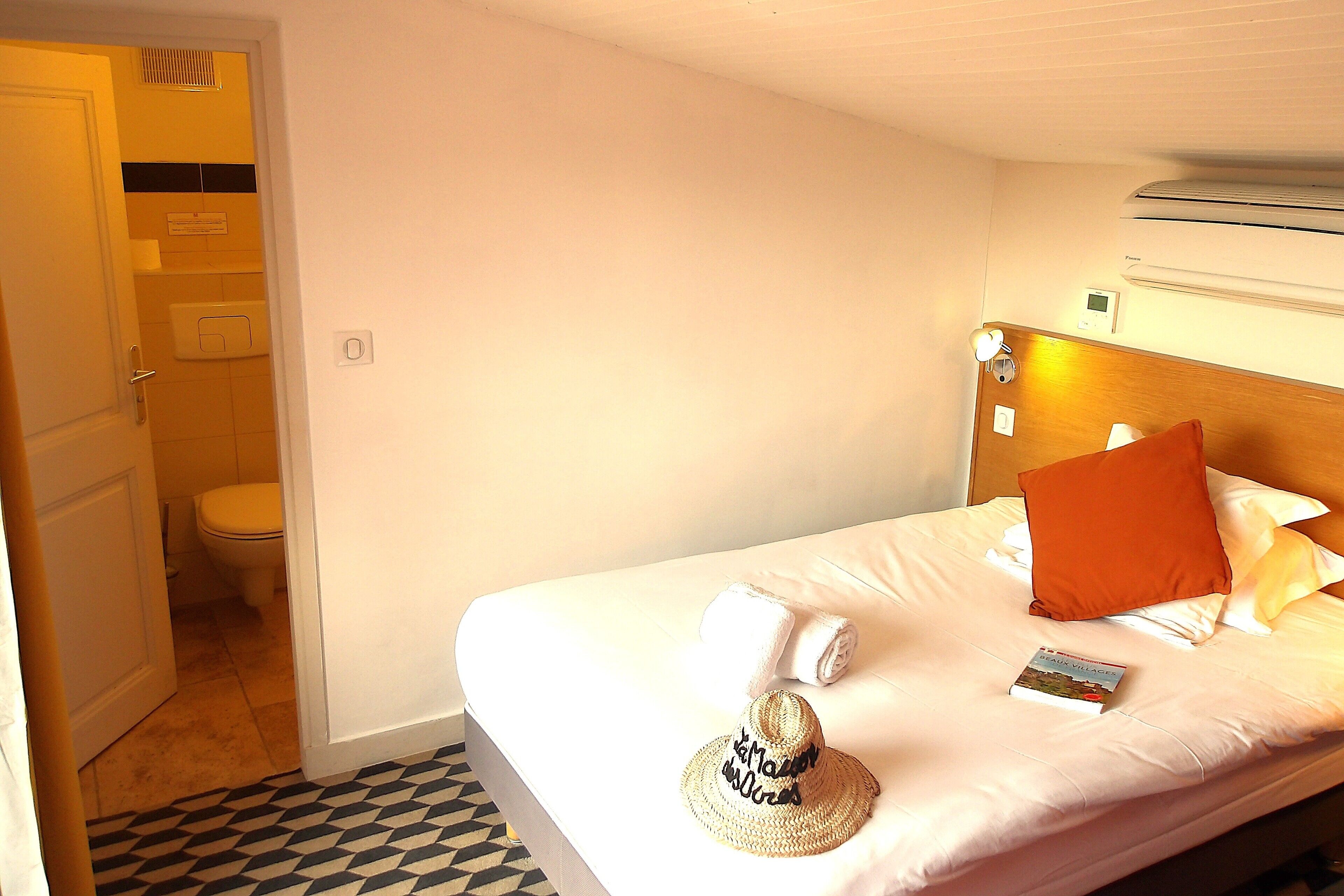 Une chambre d’hôtel avec un lit, un livre, un chapeau et une serviette posés sur le lit.