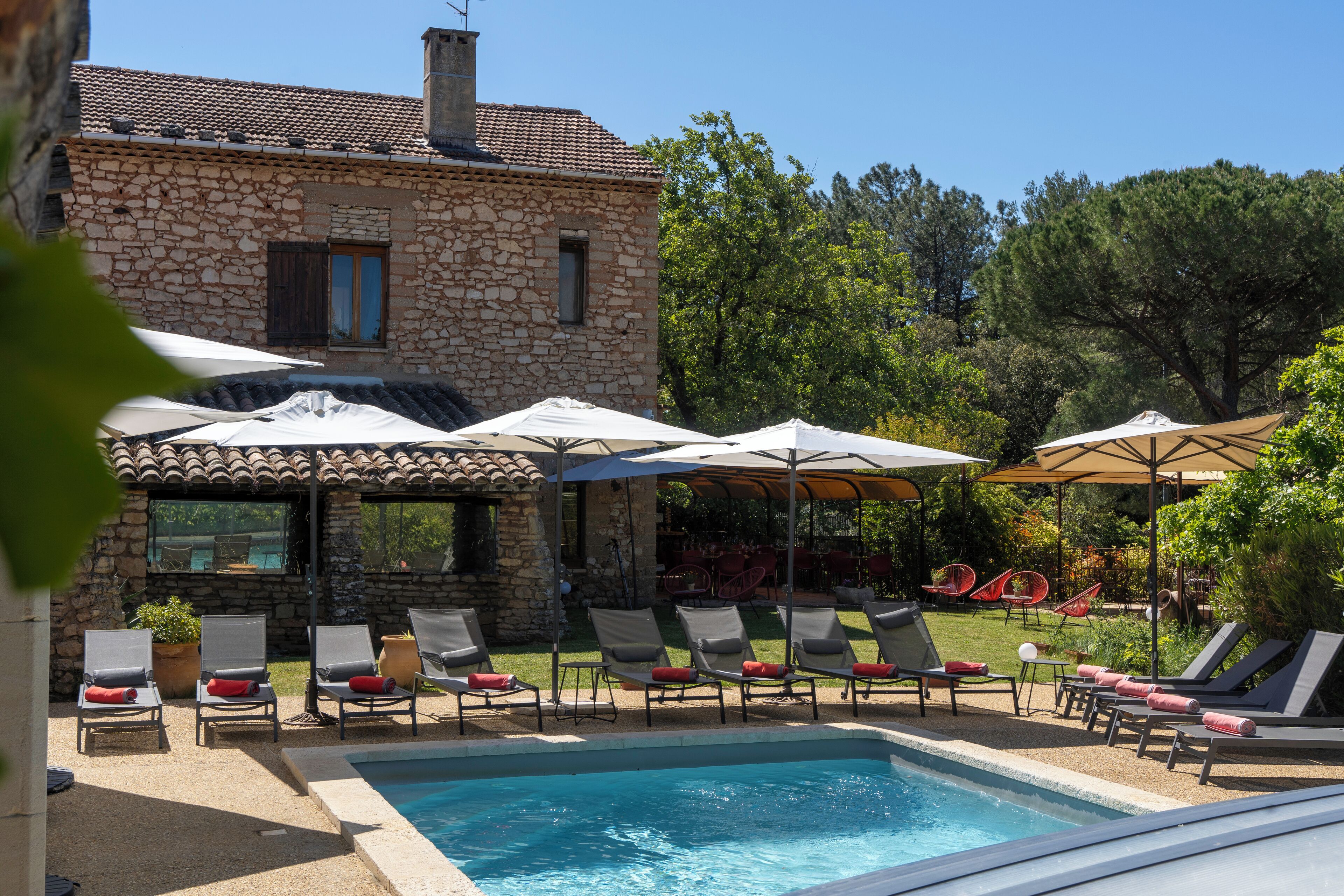 A stone building with a pool, lounge chairs, and umbrellas.
