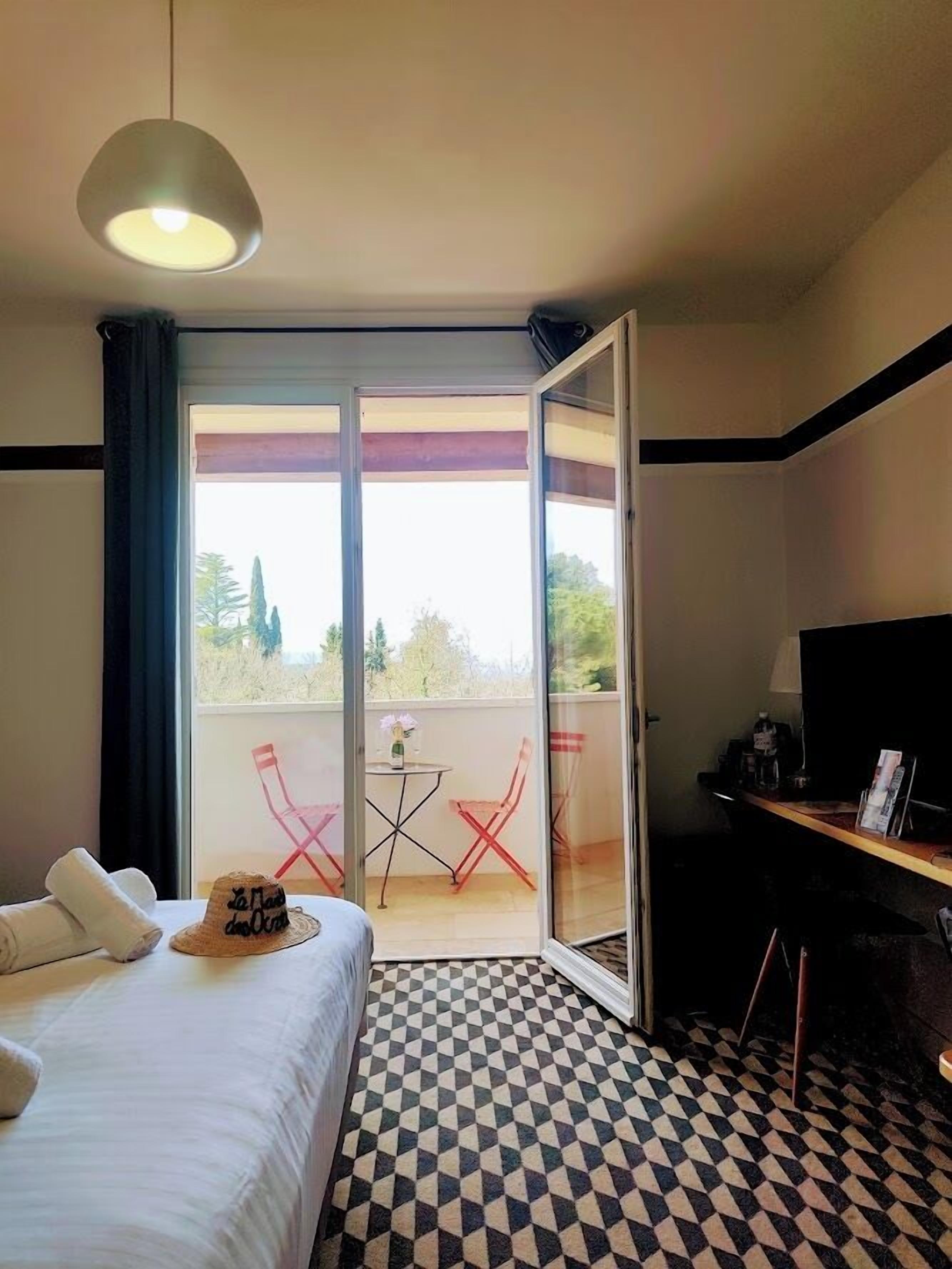 A hotel room with a bed, a TV, a balcony with a table and chairs, and a check-in counter.