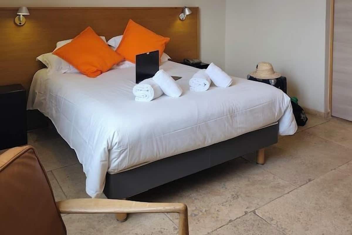 A hotel room with a bed, two bedside lamps, a nightstand, a chair, and an air conditioning unit.