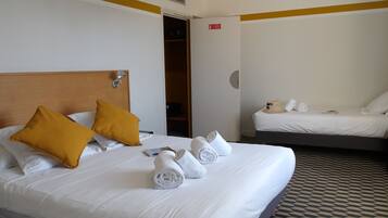 Habitació d'hotel amb dos llits, un amb almoinades grogues i l'altre amb almoinades blanques. Hi ha tovalloles ordenadament plegades sobre els llits.