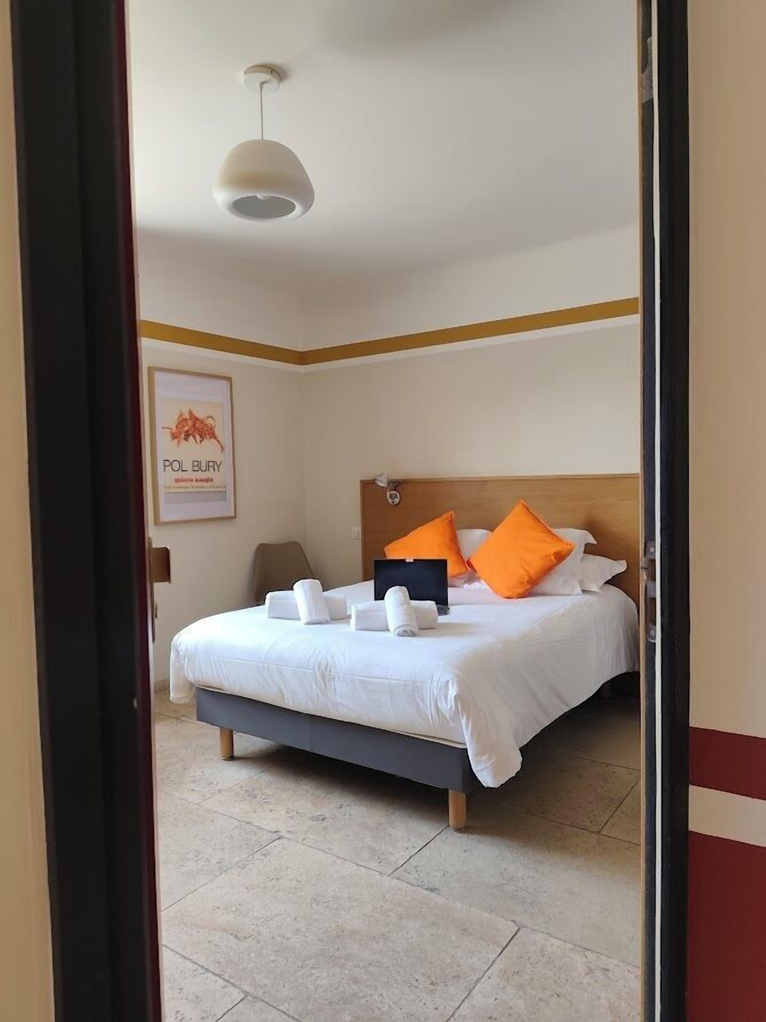 Habitación de hotel con una cama, almohadas, una mesita de noche, una lámpara y un cuadro en la pared.