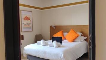 Habitación de hotel con una cama, almohadas, una mesita de noche, una lámpara y un cuadro en la pared.