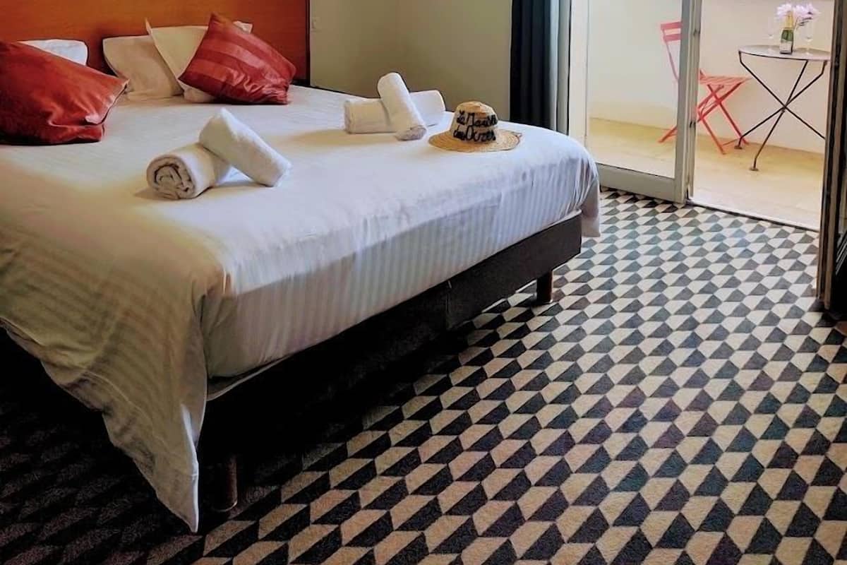A hotel room with a bed, a headboard, a large window, and a patterned floor.