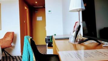 Una camera d'hotel con una reception, una scrivania con una lampada, un televisore, un pavimento decorato e una porta che dà su un'altra stanza.