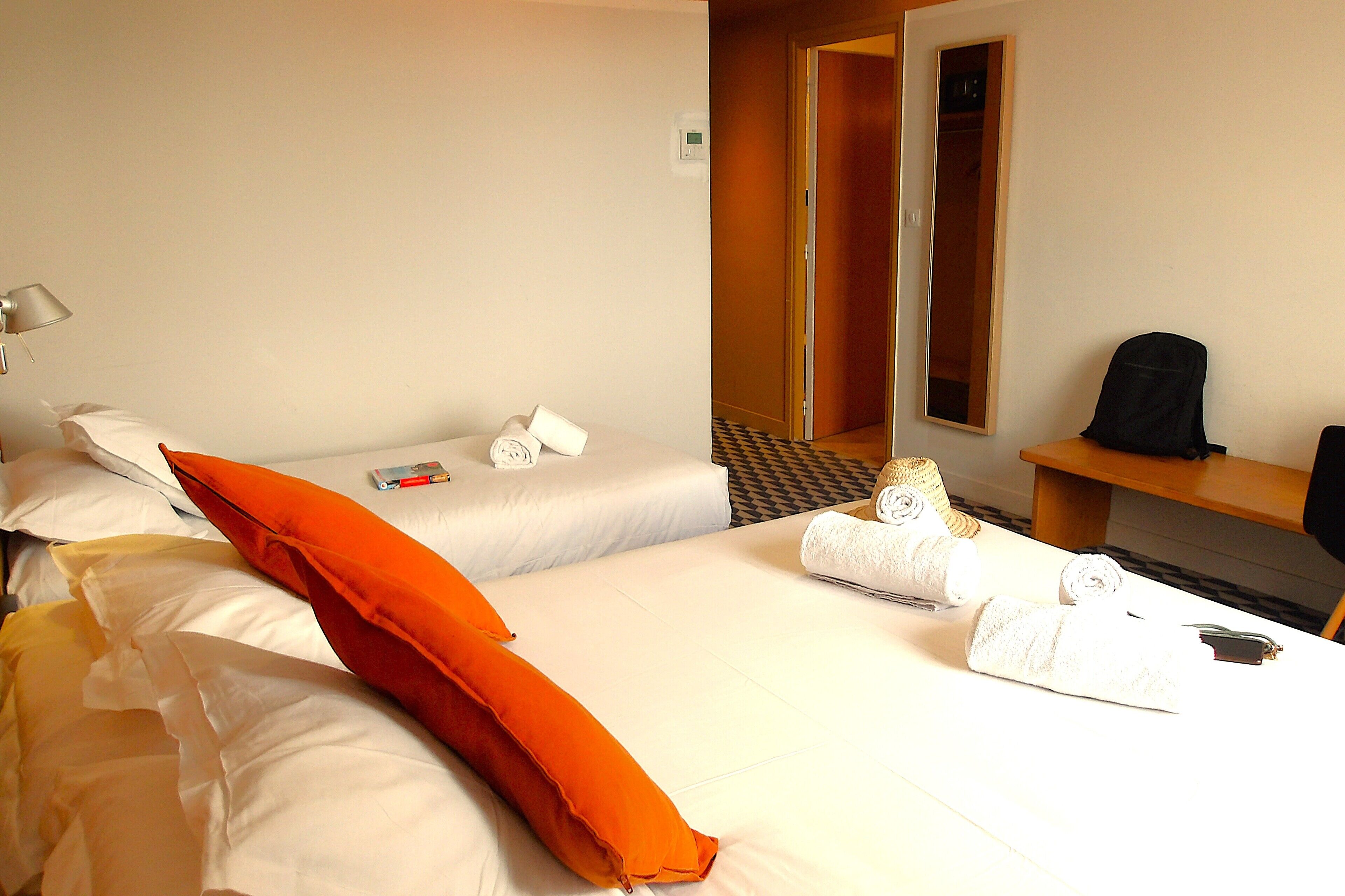 A hotel room with two beds, a desk, a chair, and a mirror.