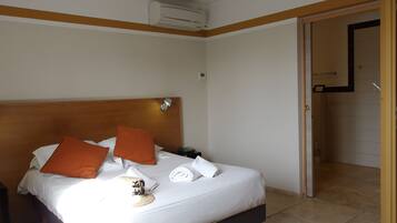 Habitación de hotel con cama, almohadas, mesita de noche, unidad de aire acondicionado y puerta que da al baño.