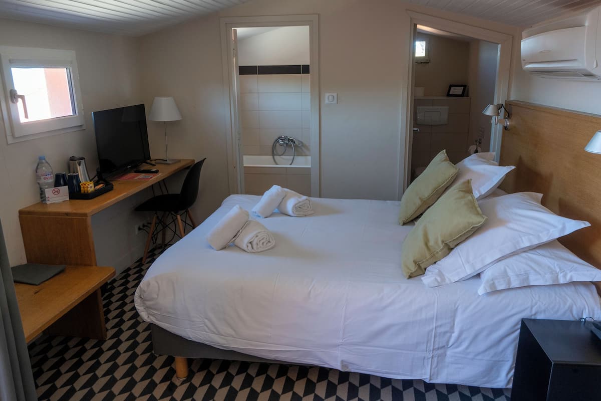 A hotel room with a bed, desk, chair, and a TV.
