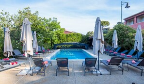 A swimming pool with lounge chairs and umbrellas, surrounded by greenery and buildings. - La Maison des Ocres (Roussillon)