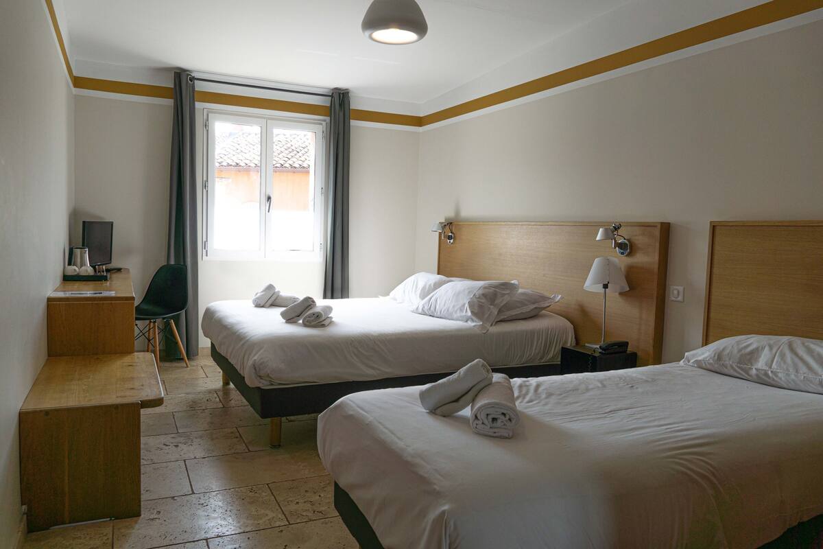 A hotel room with two beds, a desk, a chair, a TV, and a window with curtains.