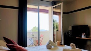 Habitación de hotel con cama, televisor, escritorio y balcón con mesa y sillas.