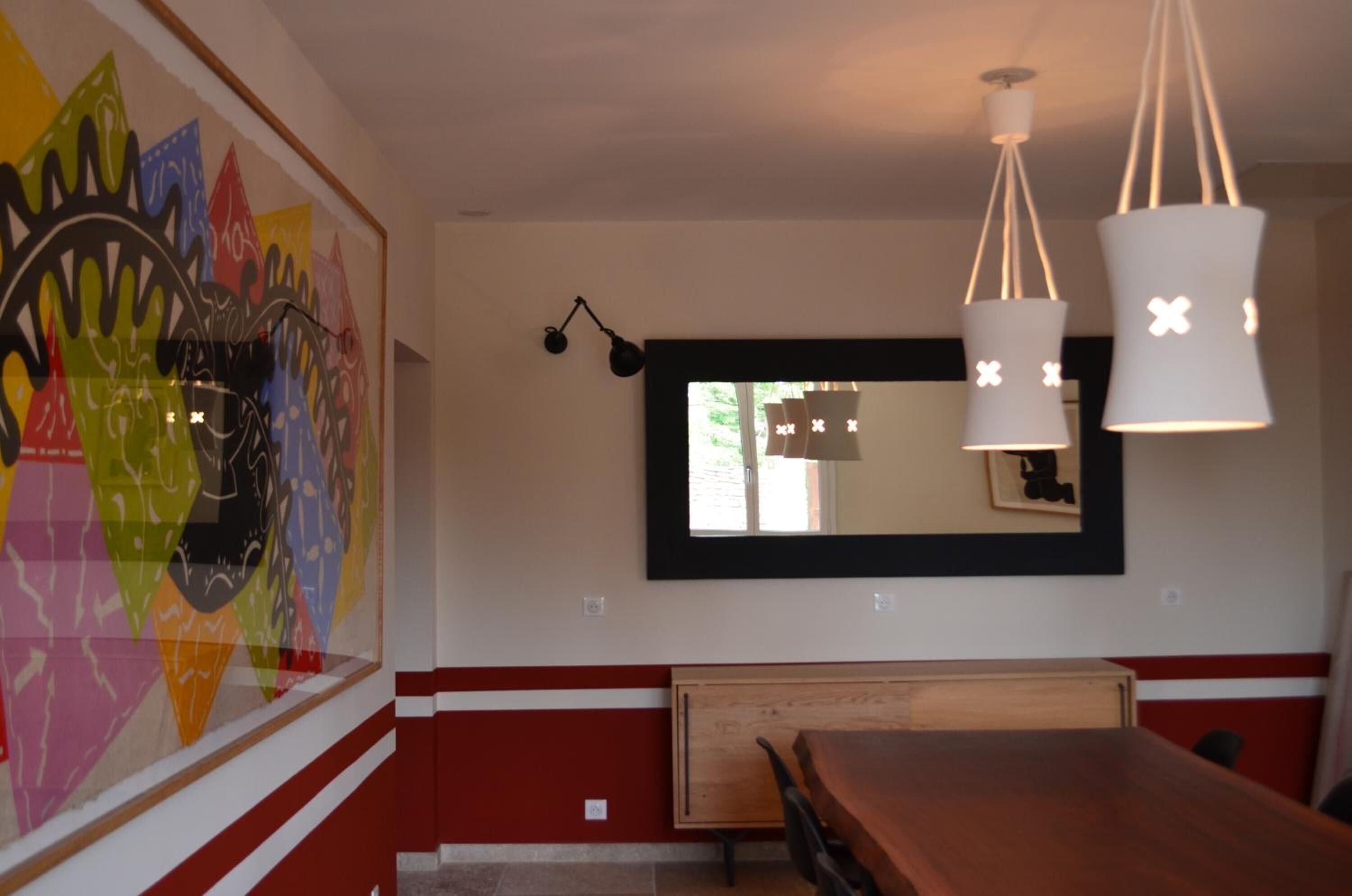 A dining area with a wooden table, a red and white wall, and a large abstract painting.
