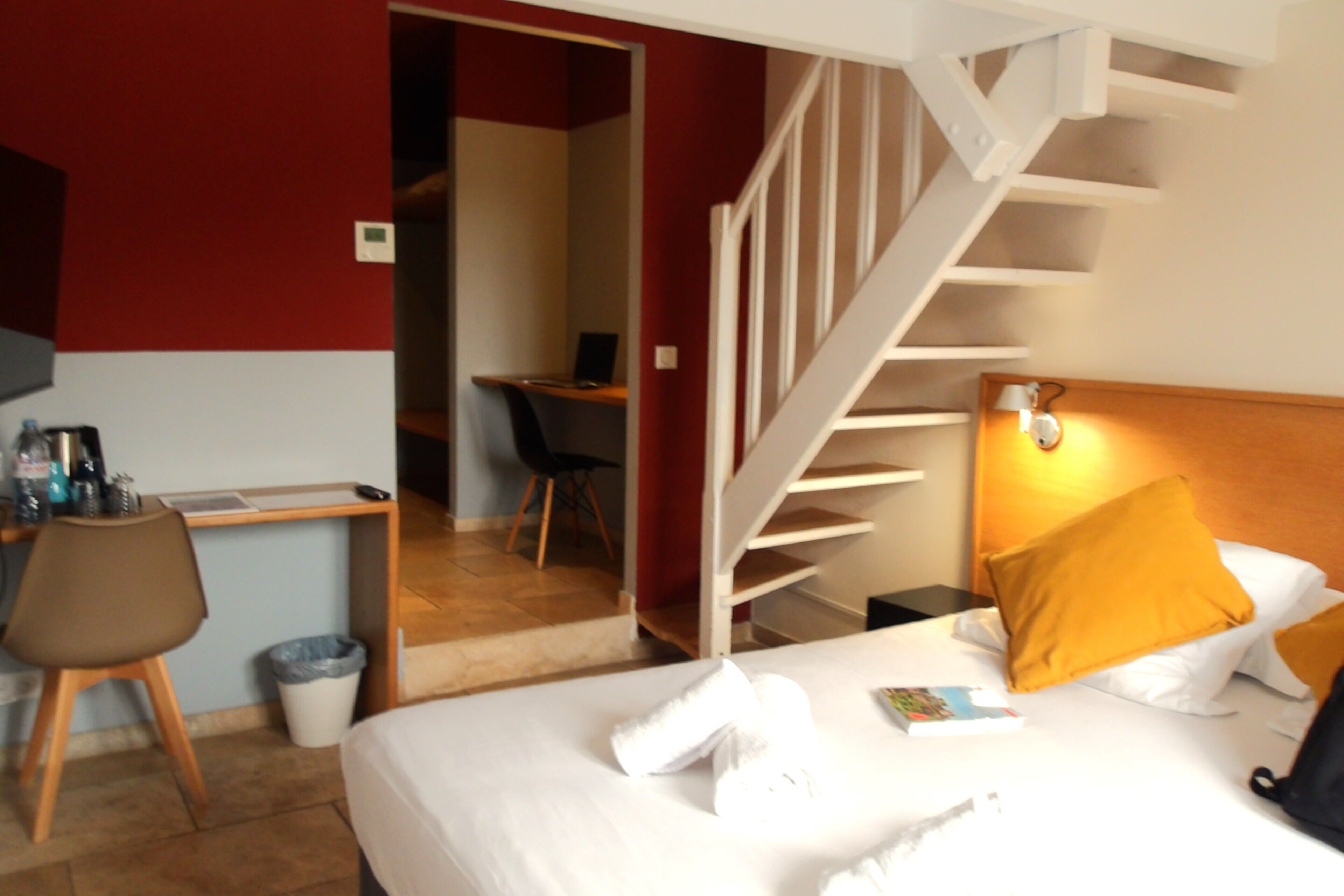 Una habitación de hotel con una cama, un escritorio, una silla y una escalera.