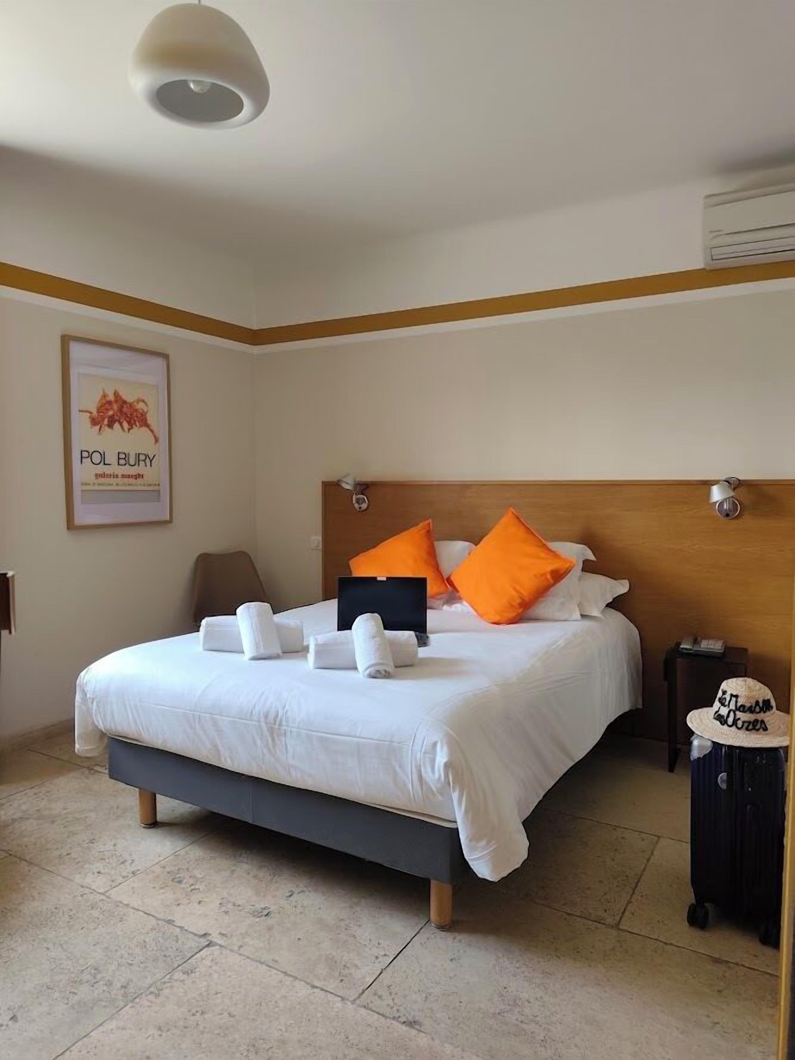 A neatly made bed with pillows, a laptop, and a suitcase, indicating a hotel room setting.