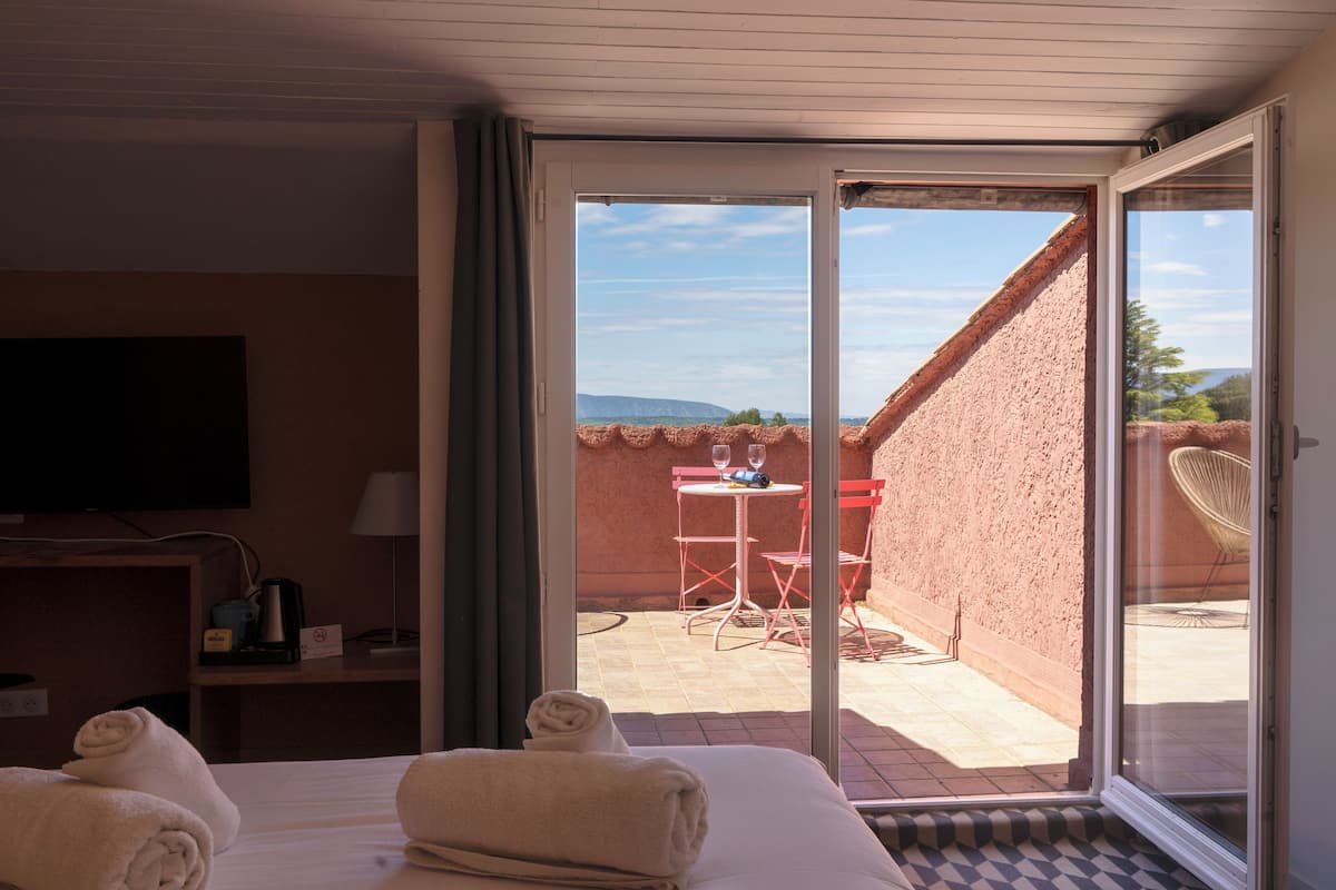 A hotel room with a bed, a TV, a desk with a lamp, and a view of an outdoor patio with a table and chairs.