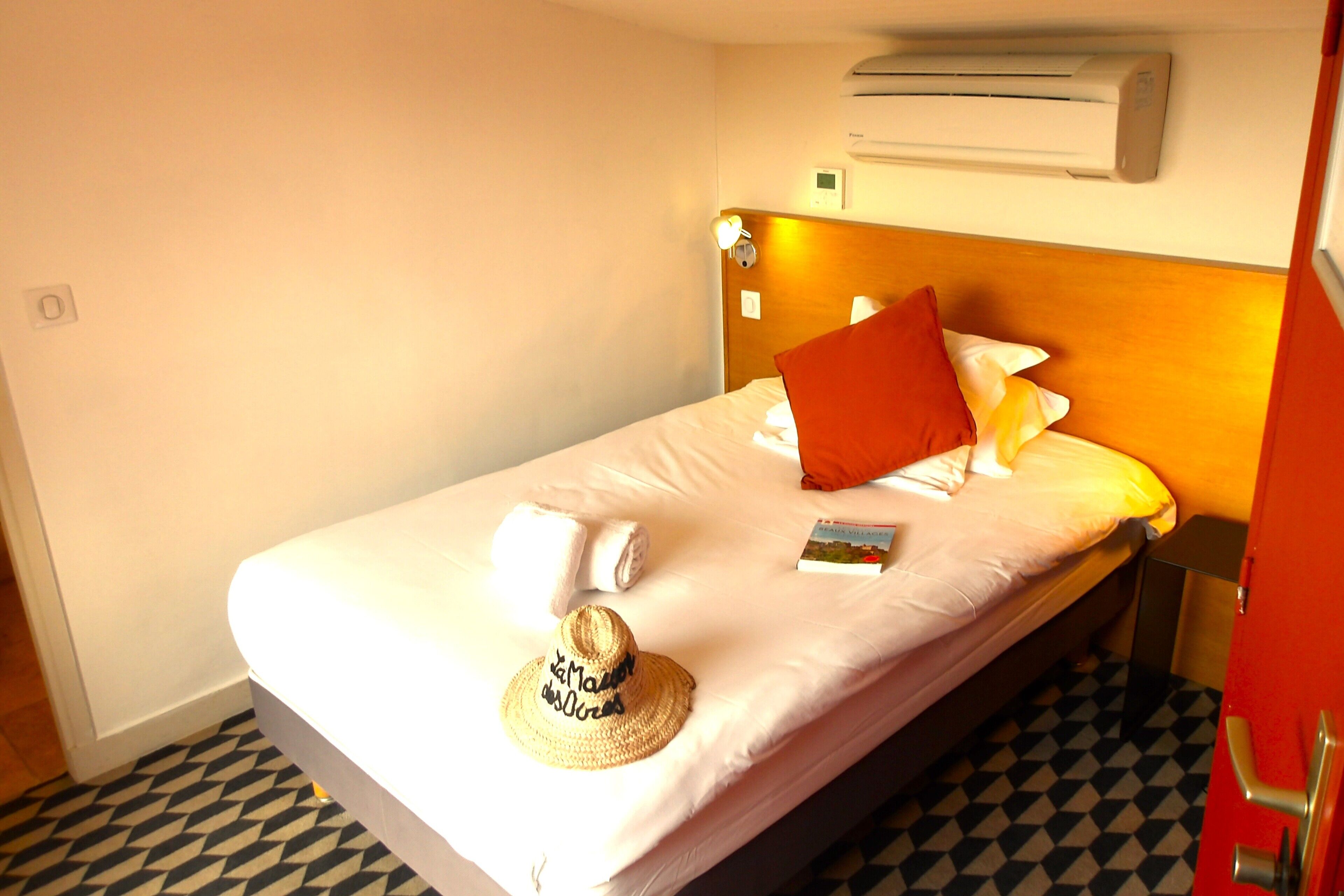 A hotel room with a bed, a wall-mounted air conditioner, a bedside table, and a patterned floor.