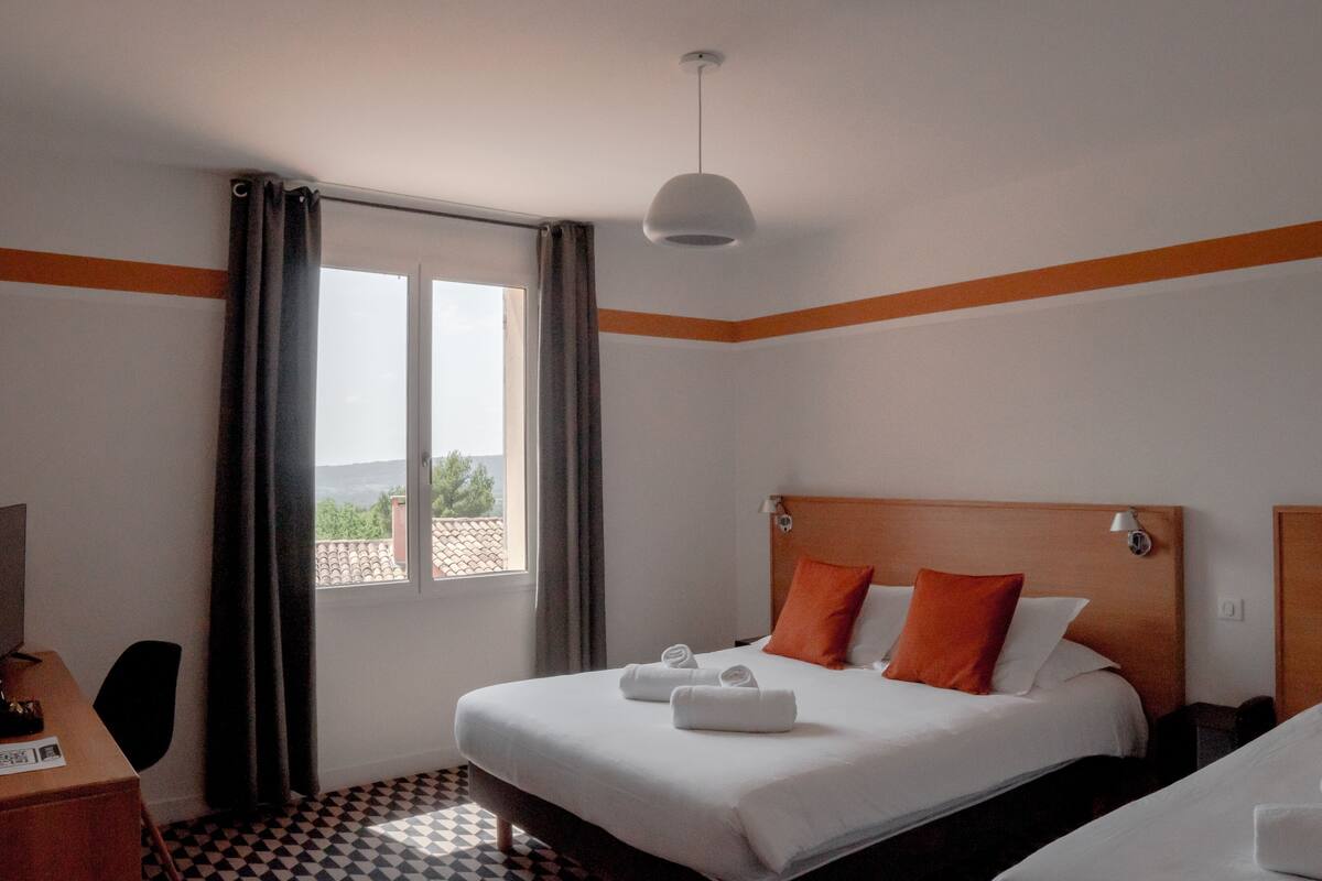A hotel room with a bed, a desk, a chair, a window with curtains, and a view of the outside.