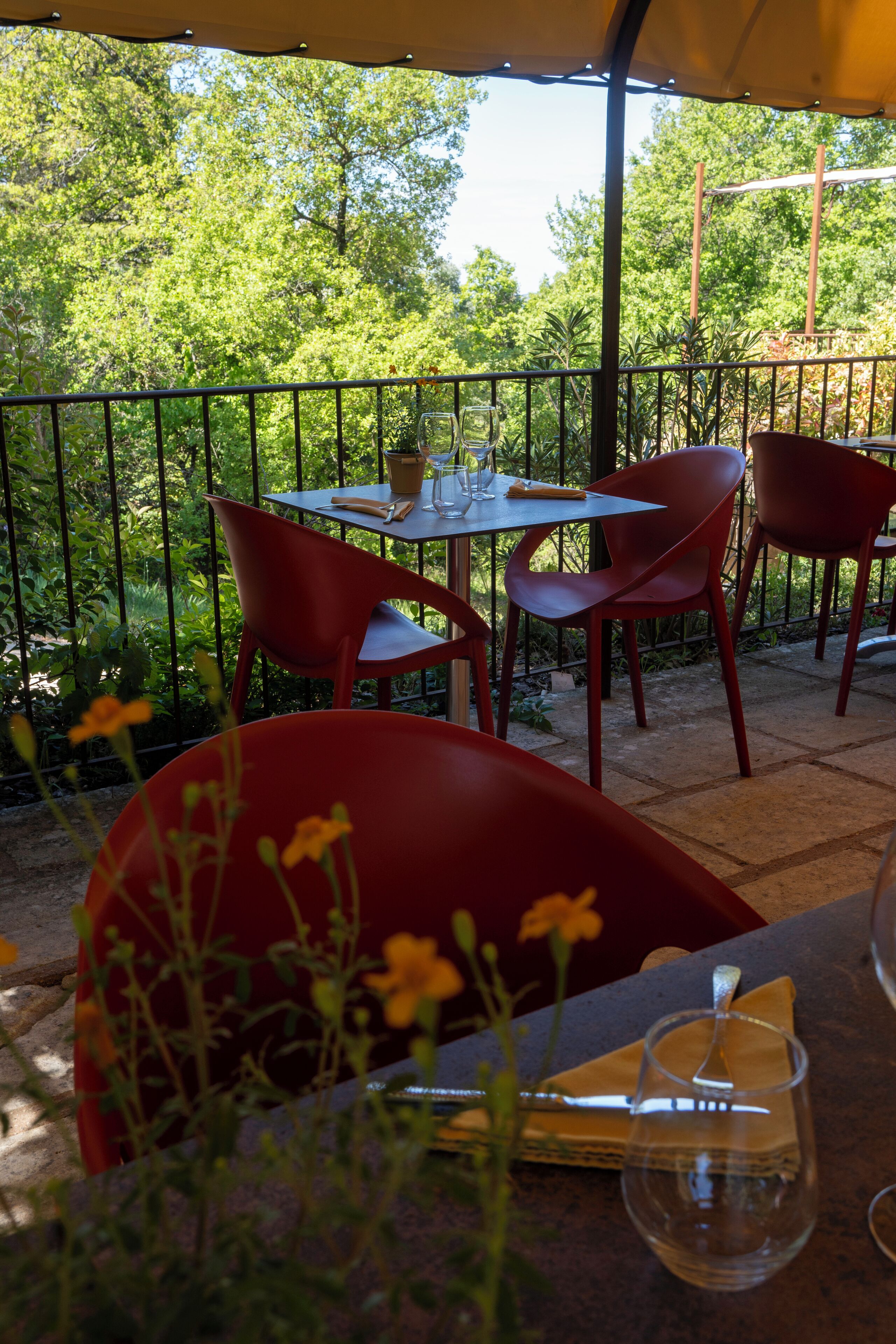 An outdoor patio with a table and chairs, surrounded by a metal fence and greenery.