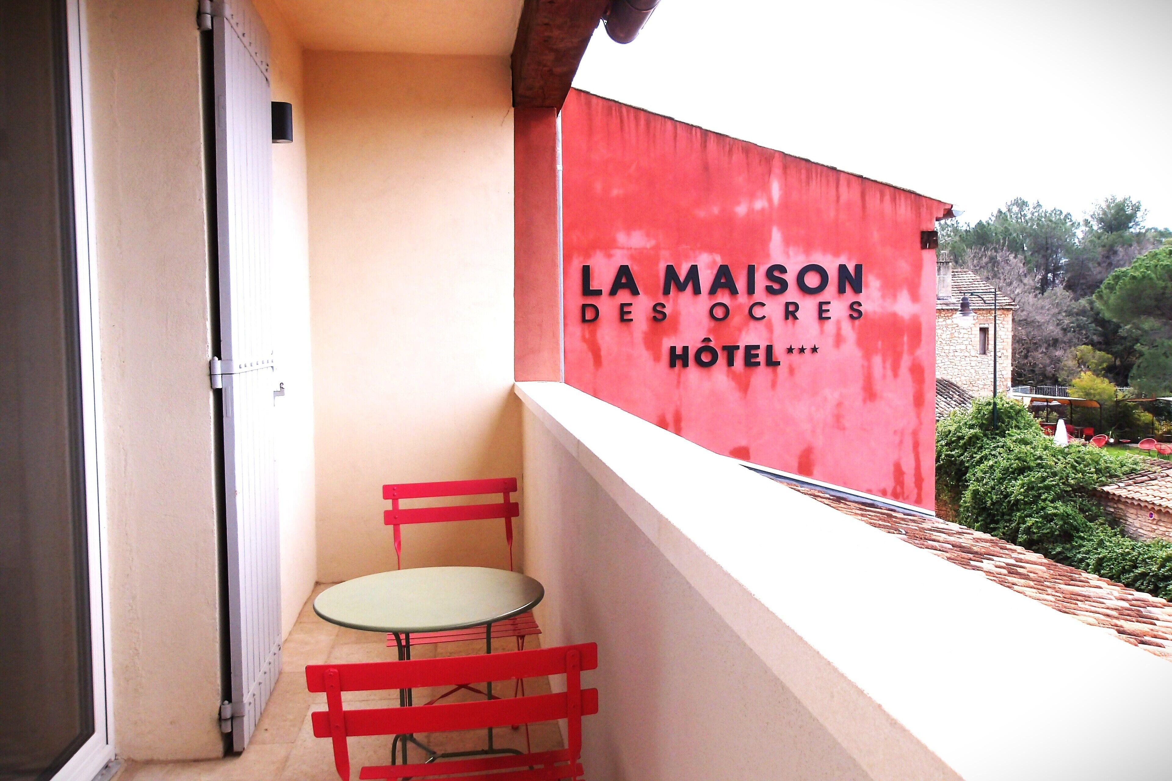 A small balcony with a red wall and a table and chair.