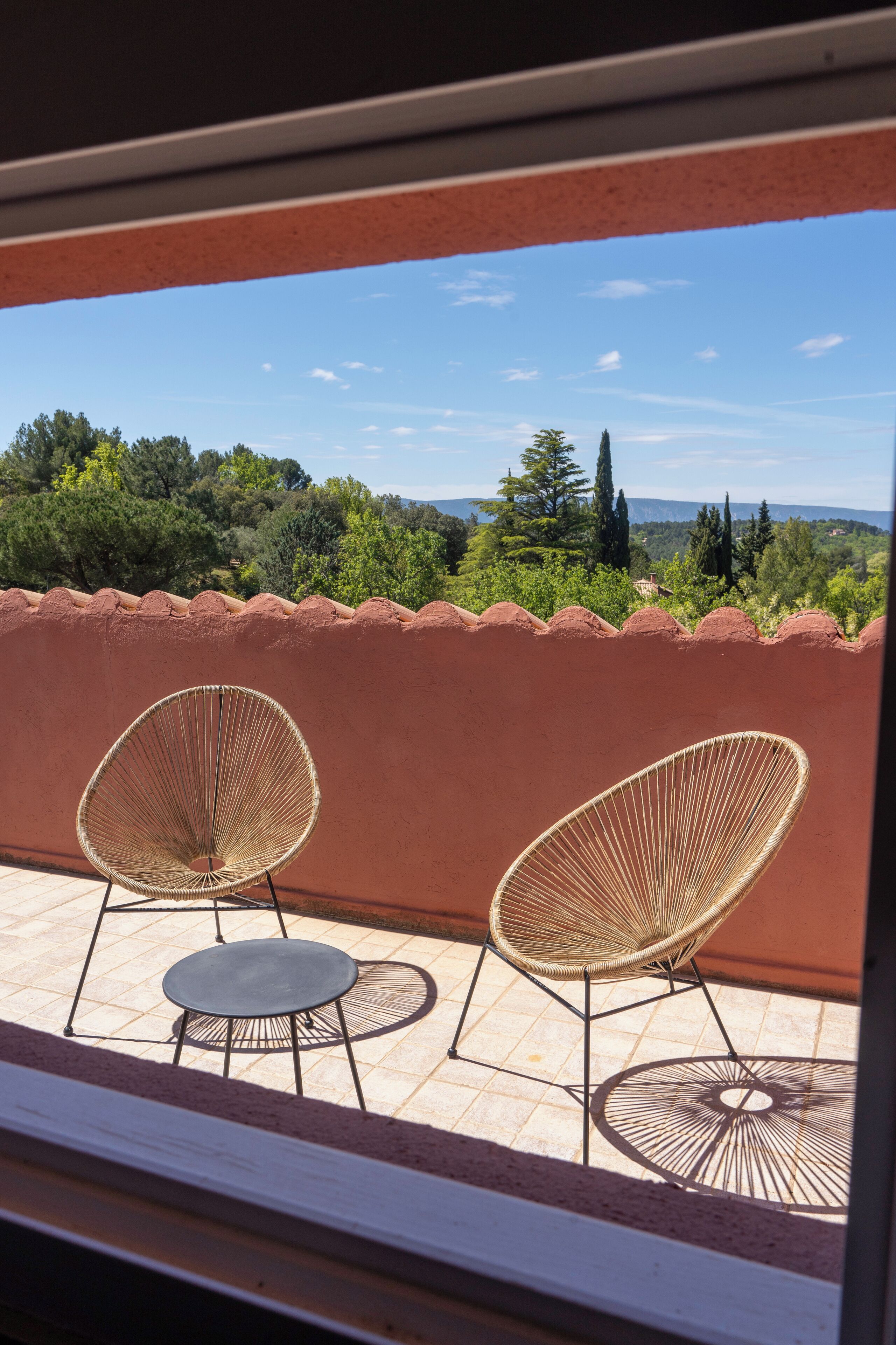 Ein Balkon mit zwei Korbstühlen und einem kleinen runden Tisch, mit Blick auf eine malerische Landschaft aus Bäumen und sanften Hügeln.