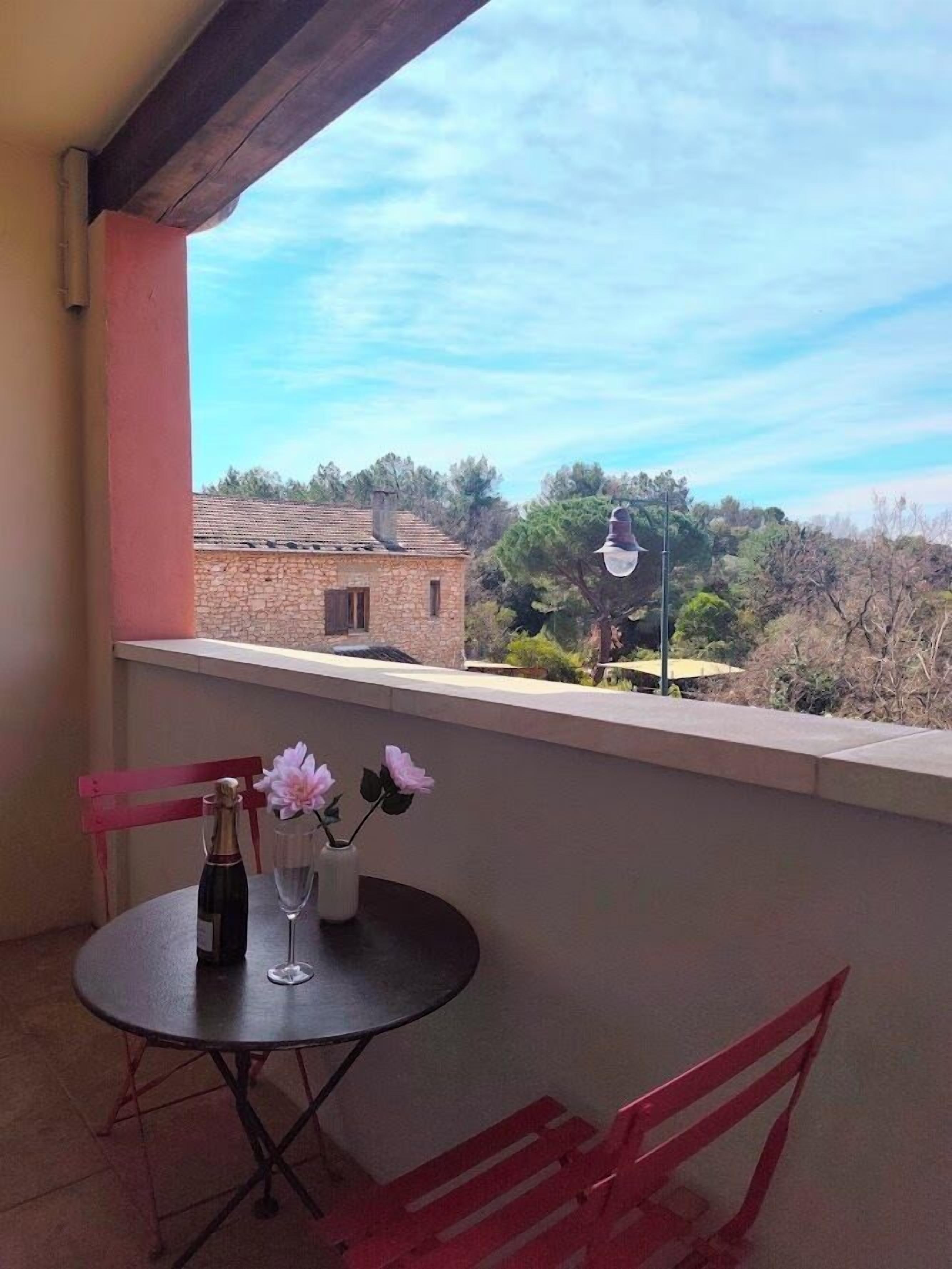 Un balcón con una mesa y sillas, una botella de champán y un florero con flores.