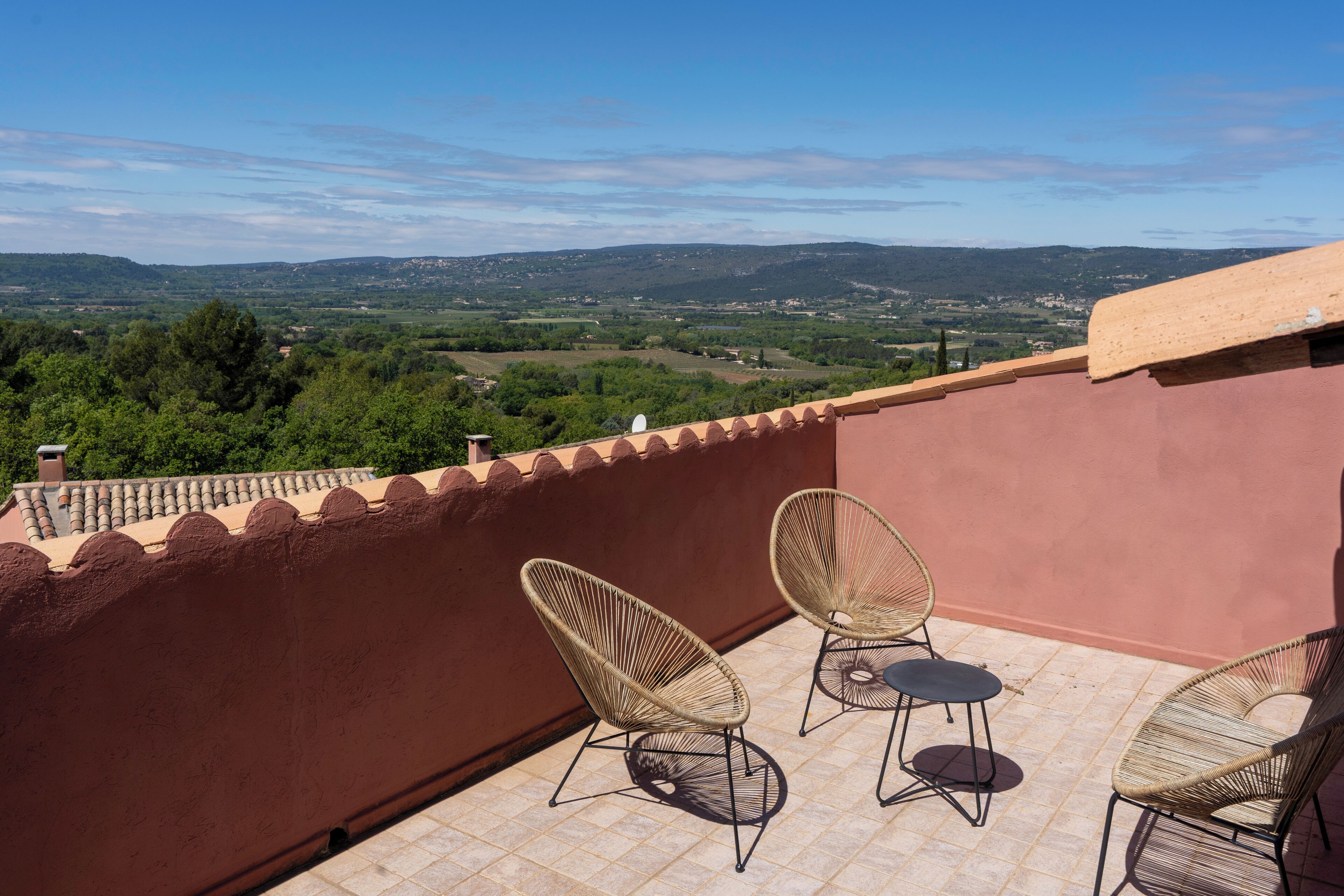 A balcony with two wicker chairs, a view of a green landscape, and a clear sky.