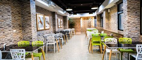 A modern dining area with stone walls, multiple tables and chairs, and framed artwork on the walls.