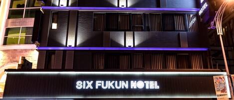 Das Six Fukun Hotel mit modernem Design, einschließlich einer auffälligen Neonreklame und einem Glastüransatz.