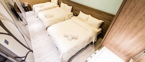 A hotel room with three beds, a wooden headboard, a small bedside table with toiletries, and a TV.