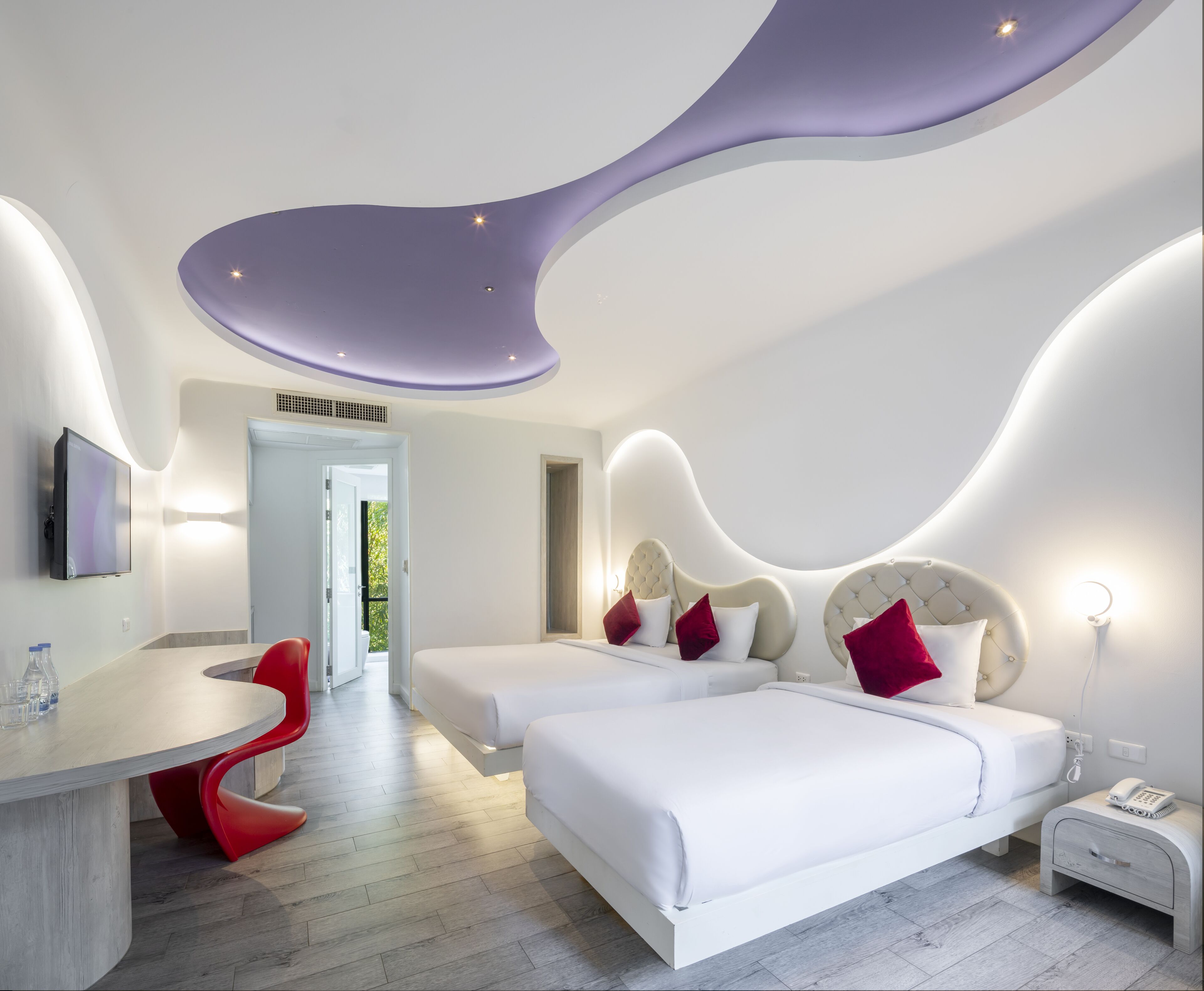 A modern bedroom with two beds, a desk, and a red chair.