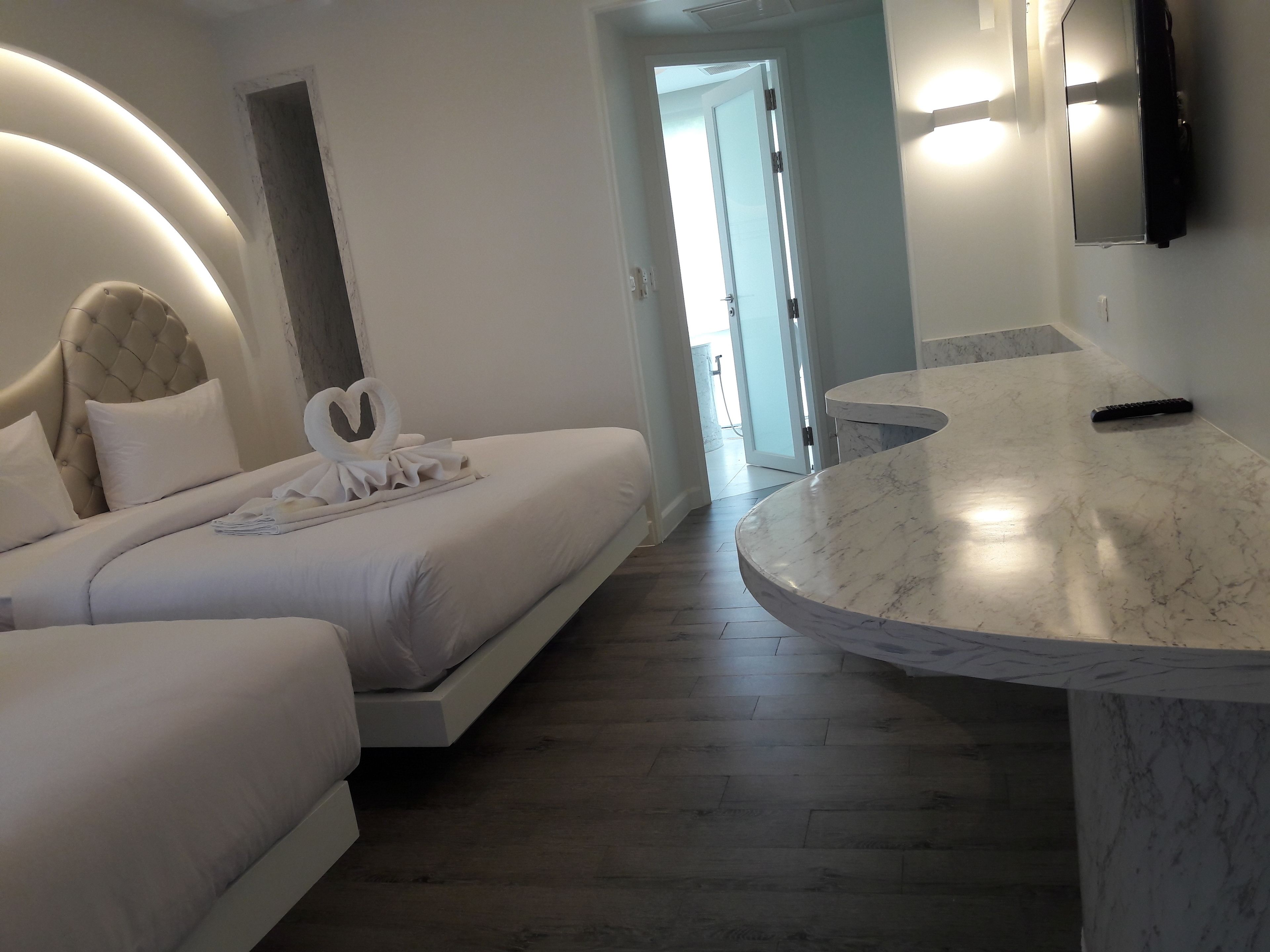 A modern hotel room with a curved marble countertop, a bed with white bedding, and a heart-shaped towel arrangement.