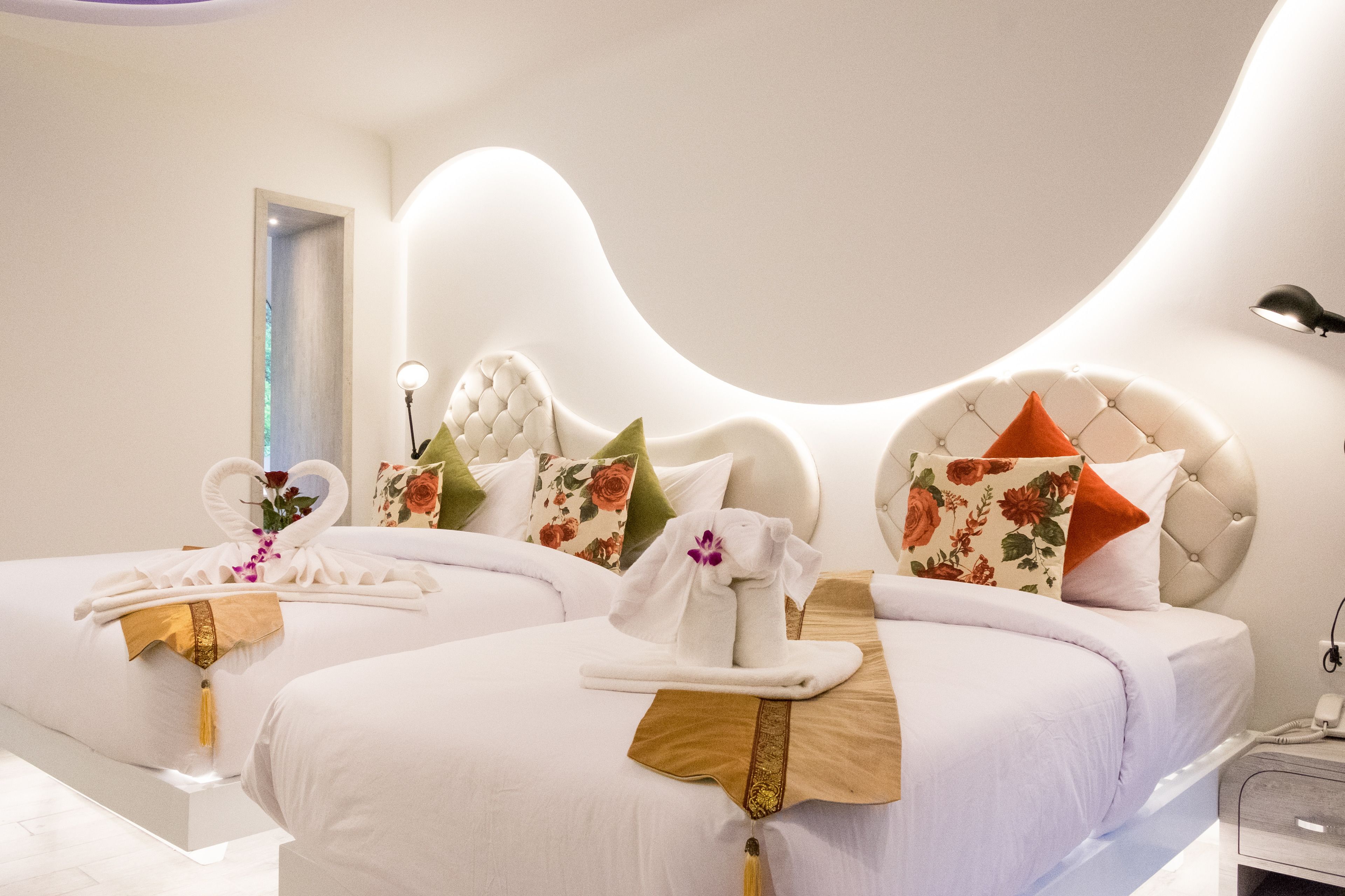 Habitación de hotel con dos camas, cada una con cubrecama blanco, toalla decorativa y almohada estampada con motivos florales.