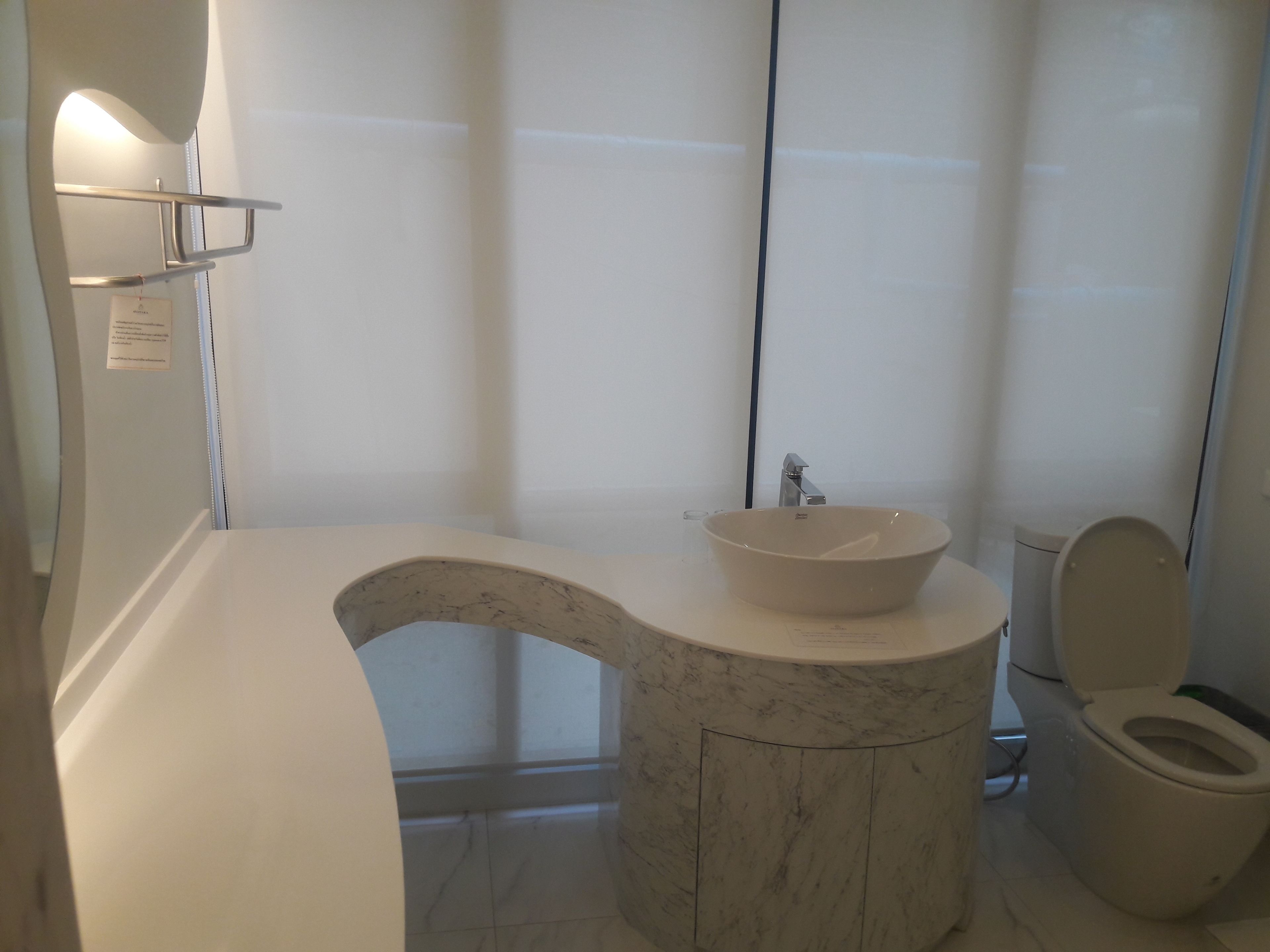 Un baño con lavamanos de mármol, inodoro y estante con espejo.