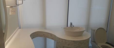 Un baño con lavamanos de mármol, inodoro y estante con espejo.