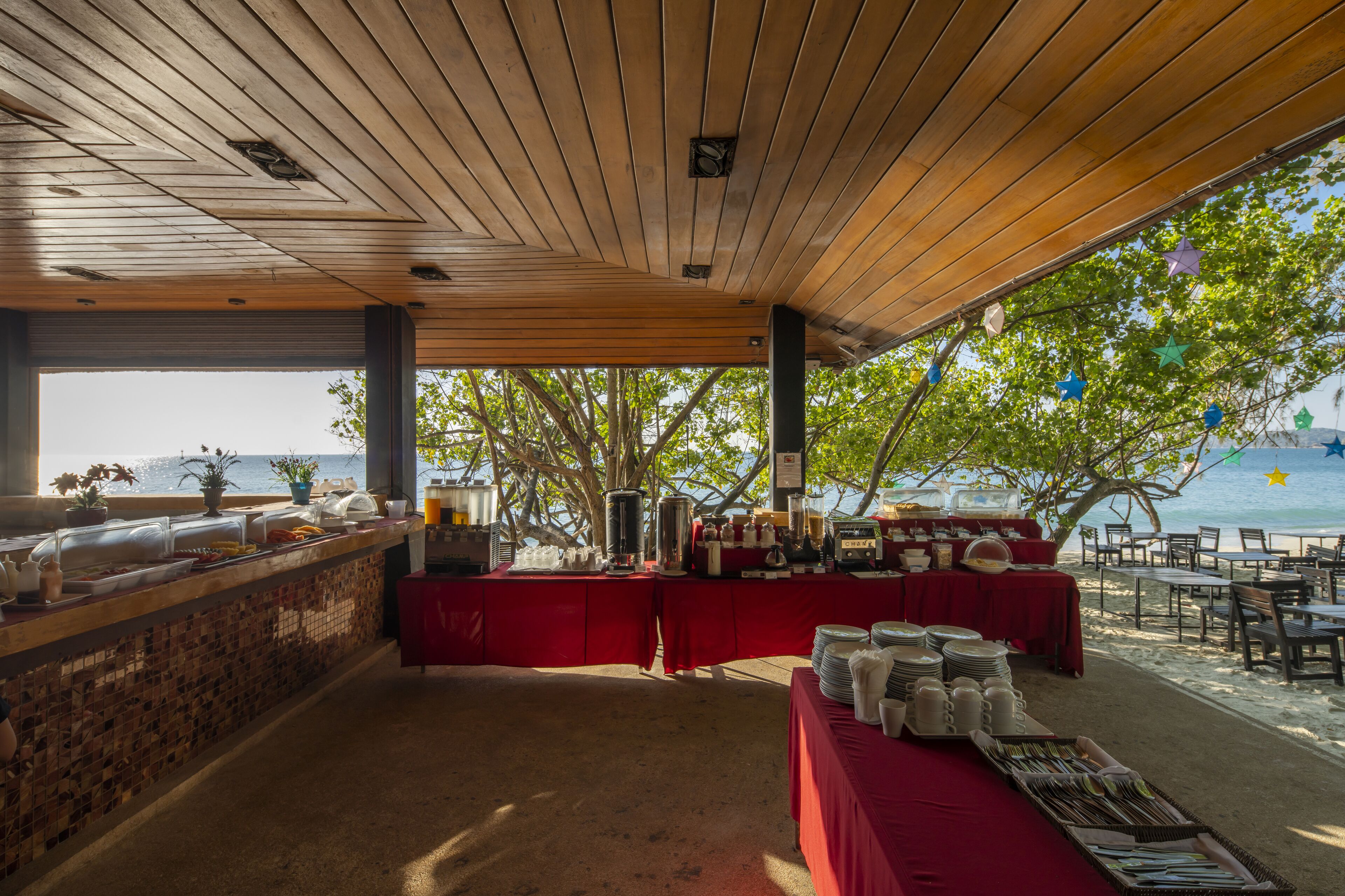 A covered outdoor dining area with a buffet setup, a view of the sea, and a wooden ceiling.