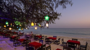 Un restaurante frente al mar con mesas y sillas, luces colgantes en forma de estrella y vistas al océano.