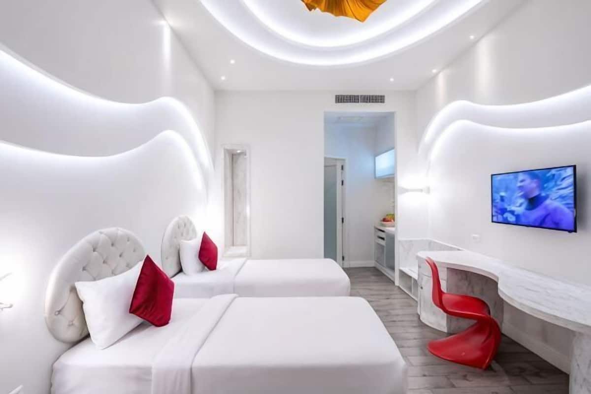 Una habitación de hotel moderna con dos camas, un televisor, una silla roja y un diseño de techo único.