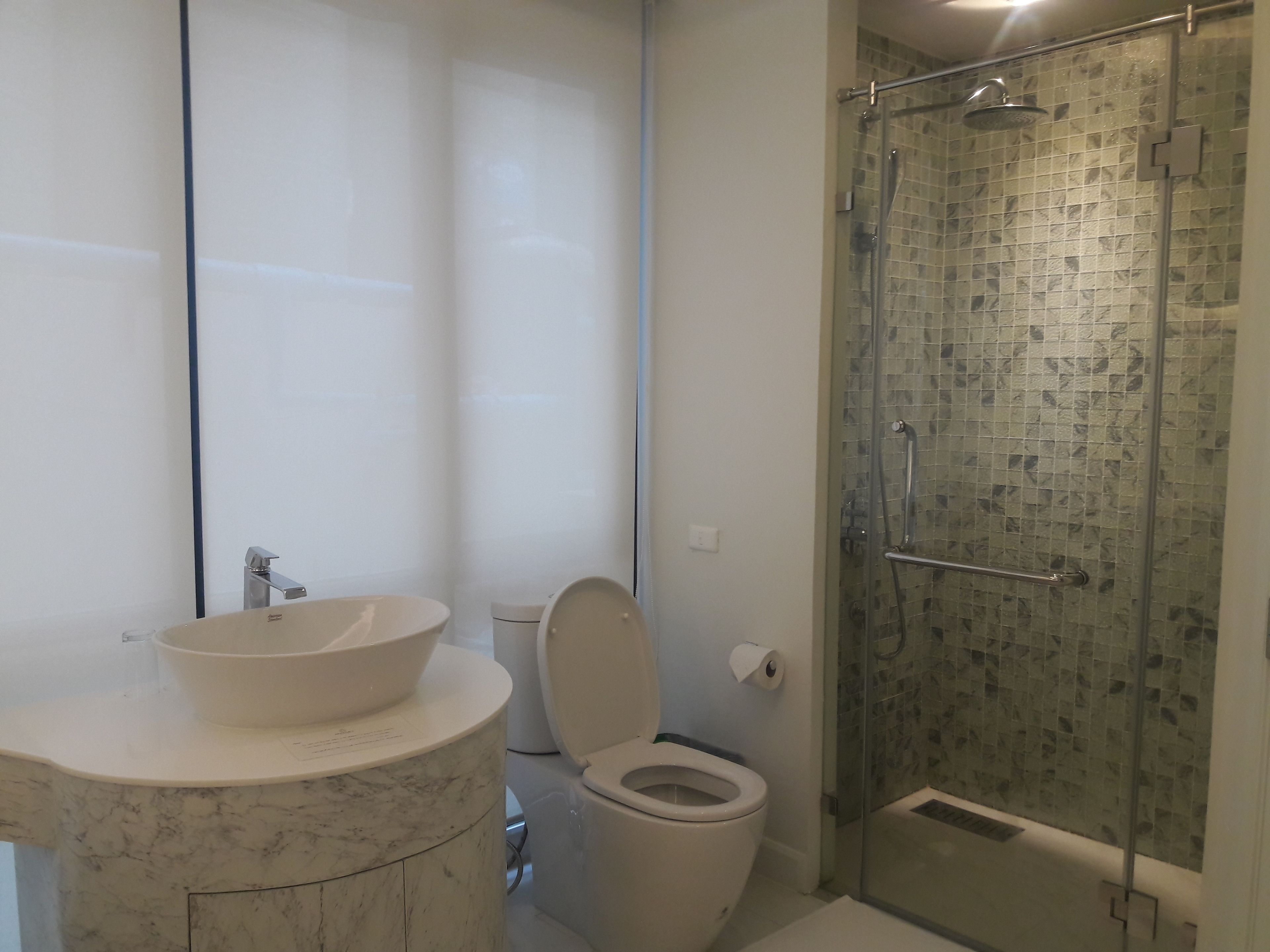 A bathroom with a glass-enclosed shower, a marble sink, and a toilet.