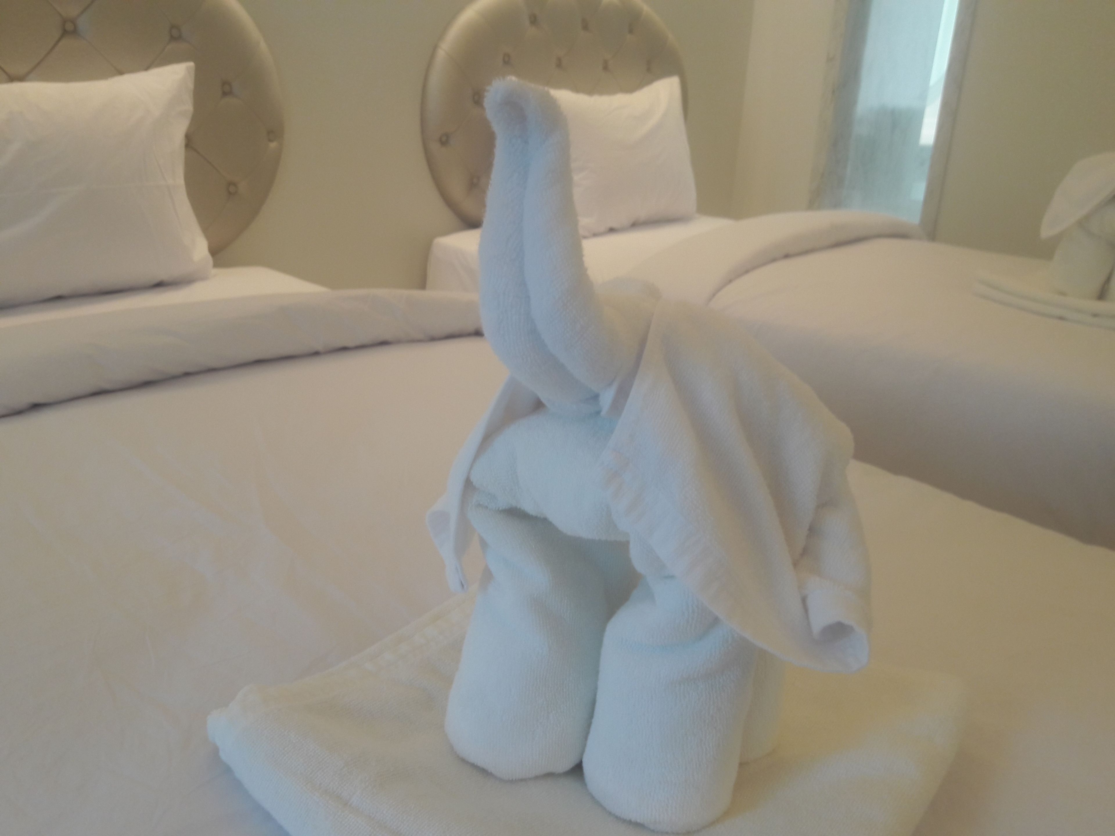 A bed with a white blanket and a towel shaped like an elephant.
