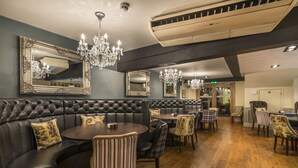A restaurant with a leather booth seating area, round tables, and chandeliers. - The Golden Lion Hotel, St Ives, Cambridgeshire (St Ives)