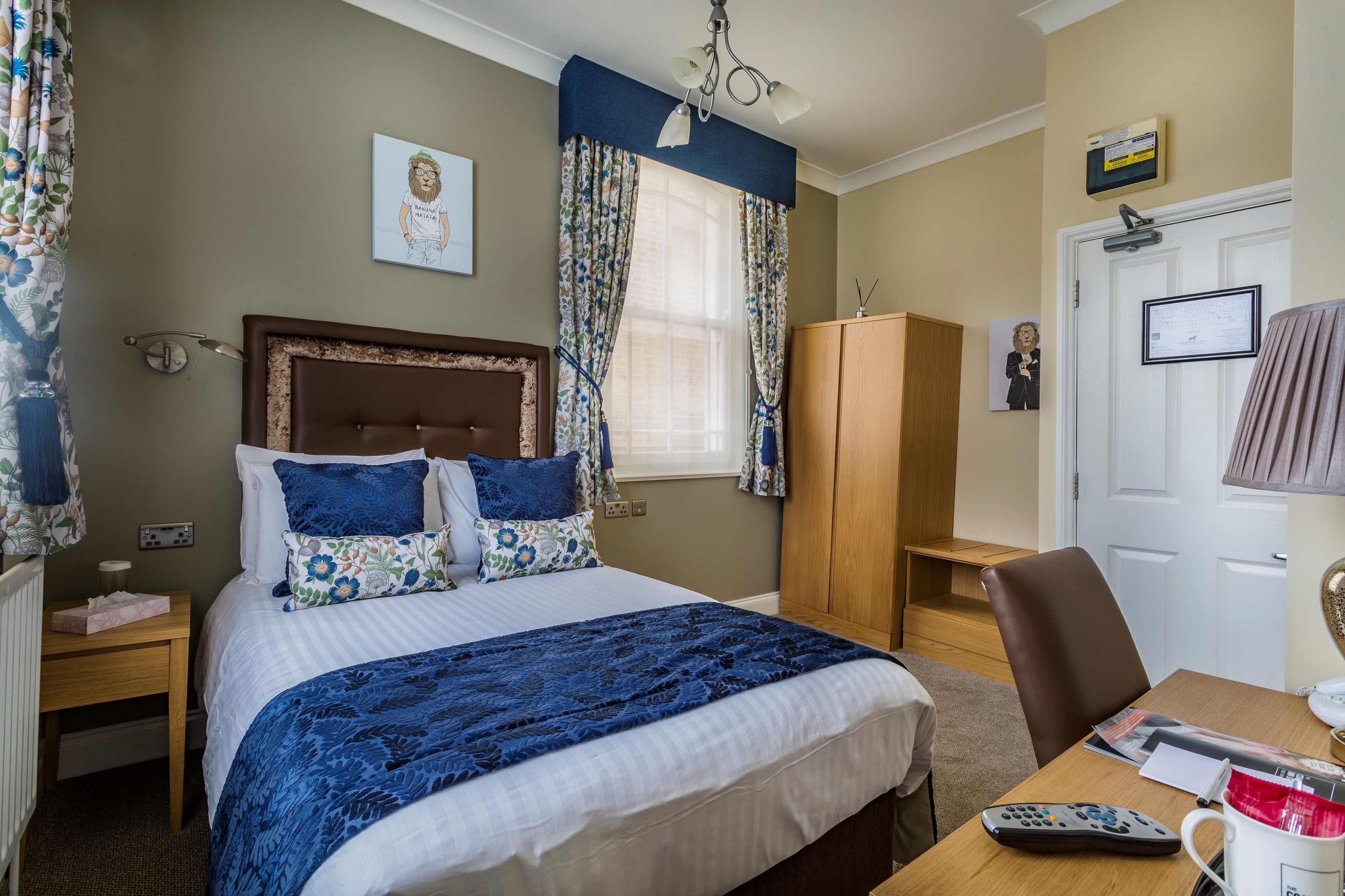 A neatly arranged bedroom with a bed, a wooden nightstand, a desk with a chair, a wardrobe, and a door with a lock.