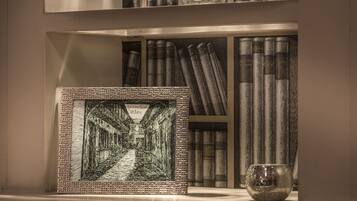 A framed artwork of a street scene, bookshelves with books, and a decorative glass object on a shelf.