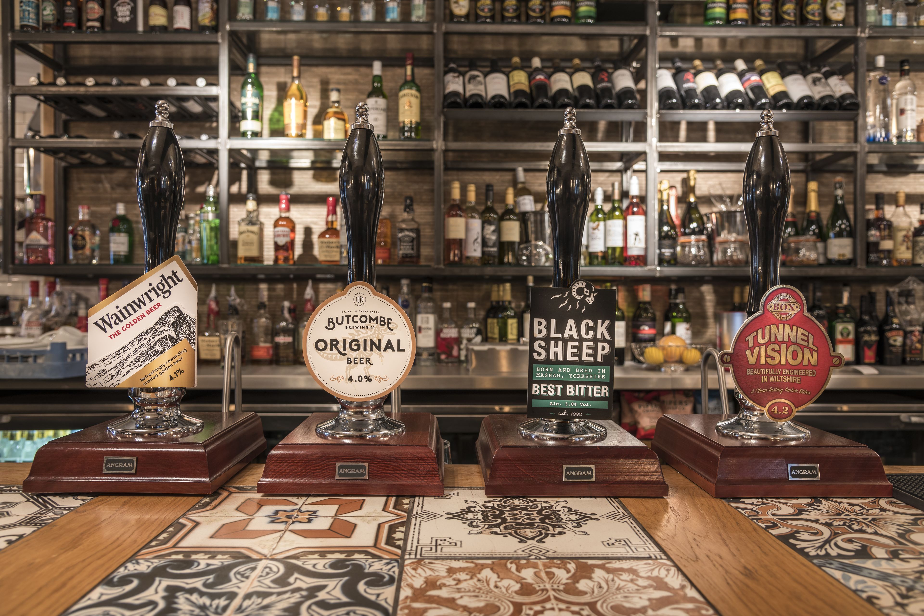 Cuatro grifos de cerveza en la barra, con estantes al fondo llenos de diferentes botellas.